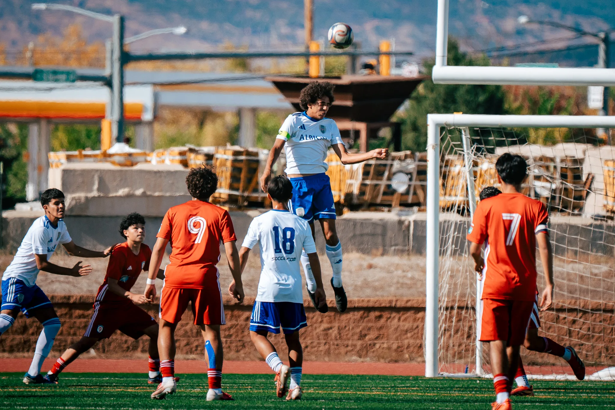 An Albion SC Colorado player in a captain's armband rises for a high ball as Albion number 18 and AC River numbers 9 and 7 look on