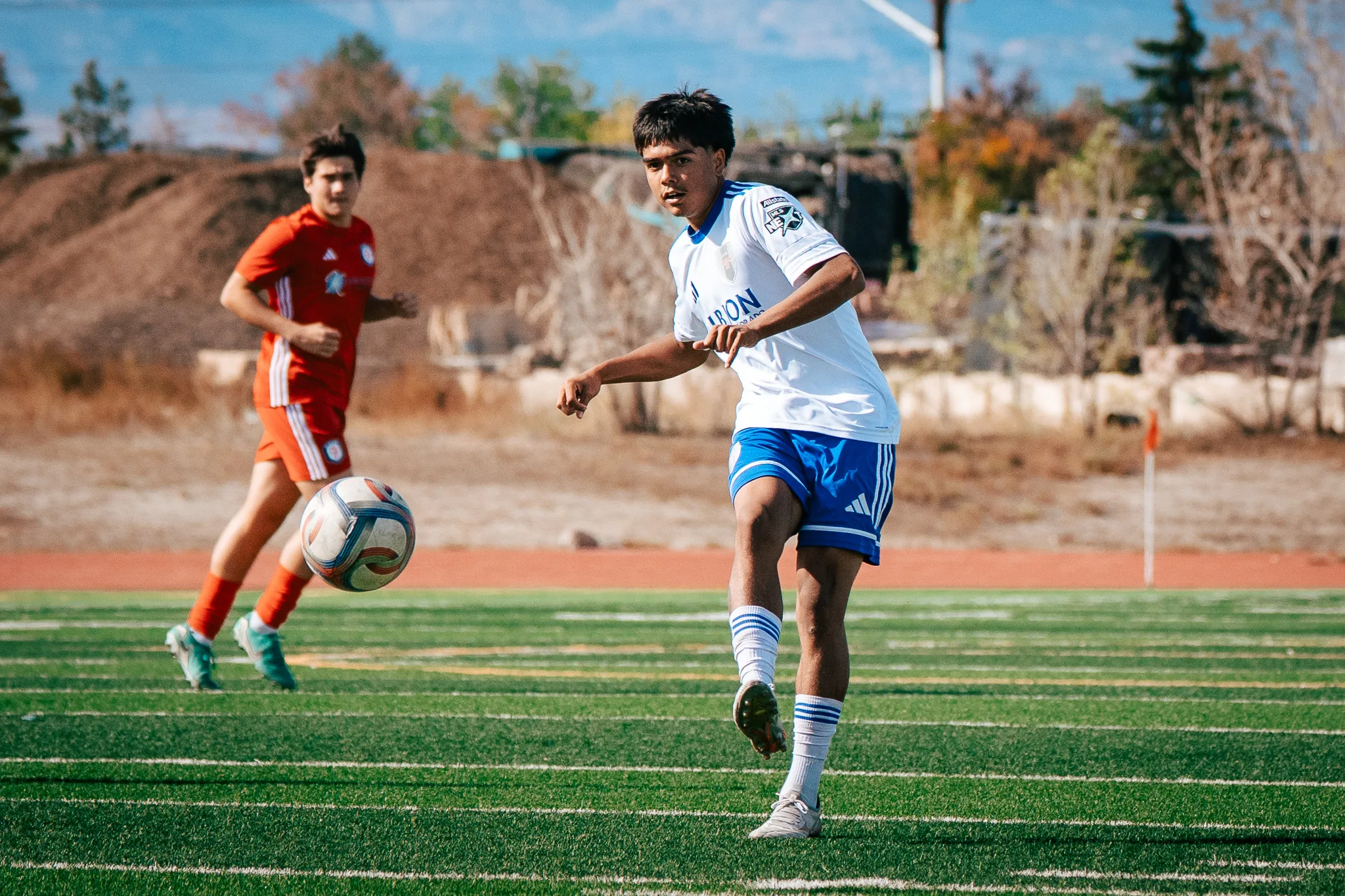An Albion SC Colorado player follows through on a pass as an AC River player runs in behind the ball