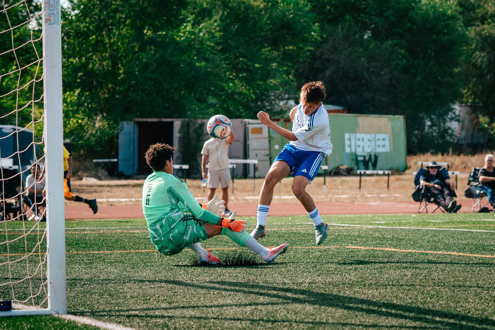 The AC River goalkeeper in green slides out as an Albion SC Colorado player gets his kick away, the ball flying past