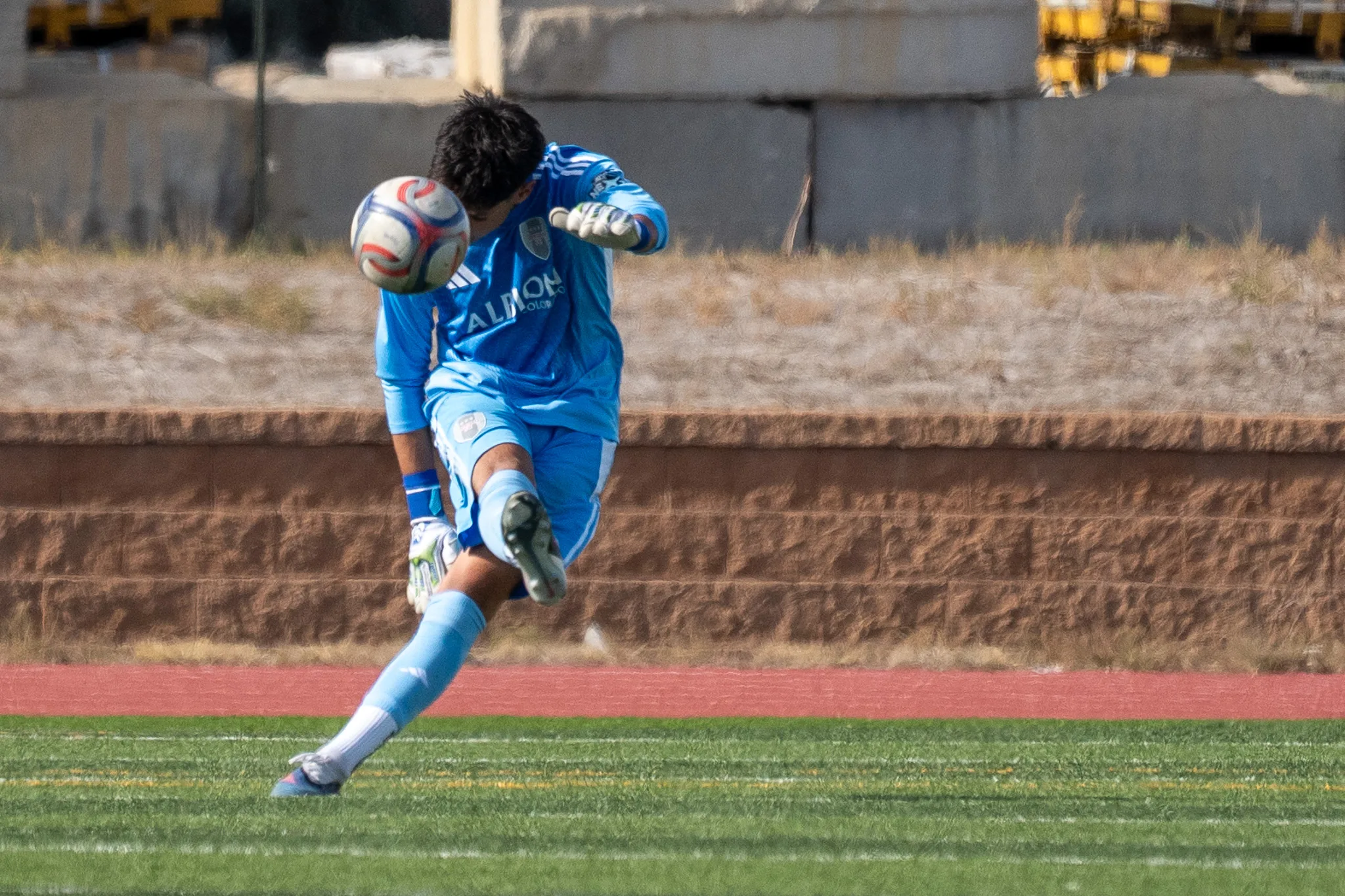 The Albion SC Colorado goalkeeper in light blue punts the ball, his eyes on it