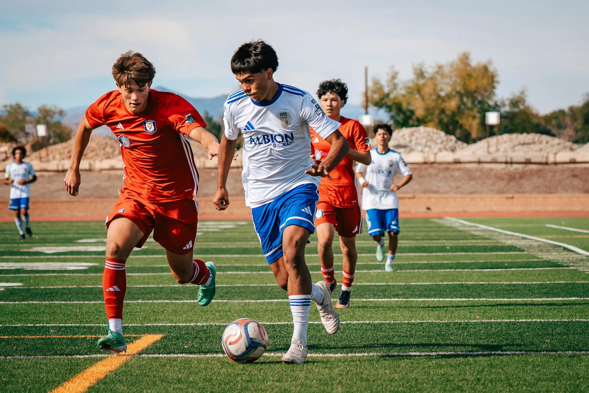 An Albion SC Colorado player pushes the ball ahead as AC River players chase on both sides