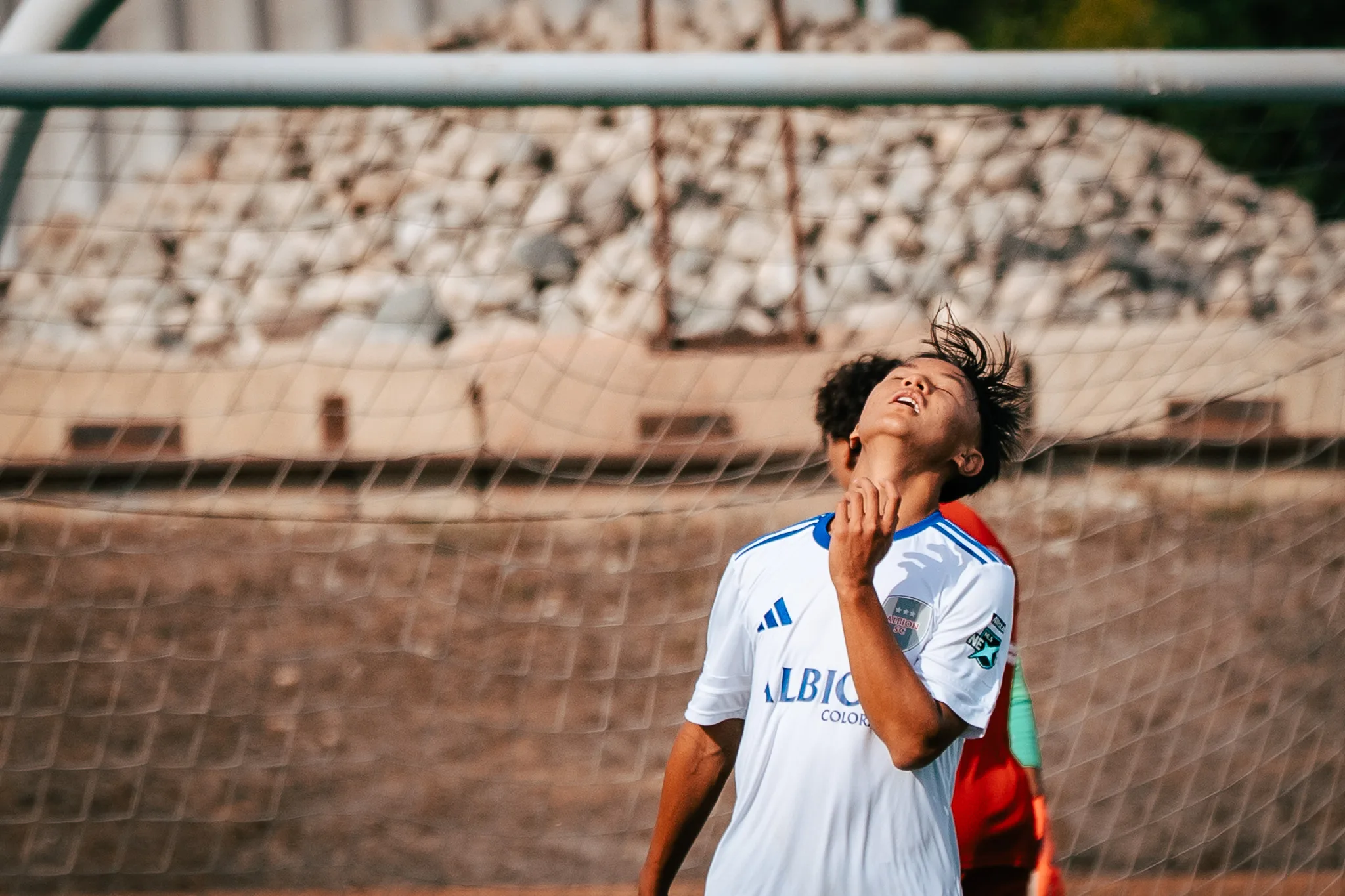 In front of the goal net, an Albion SC Colorado player tips his head back with his eyes closed and a hand at his collar