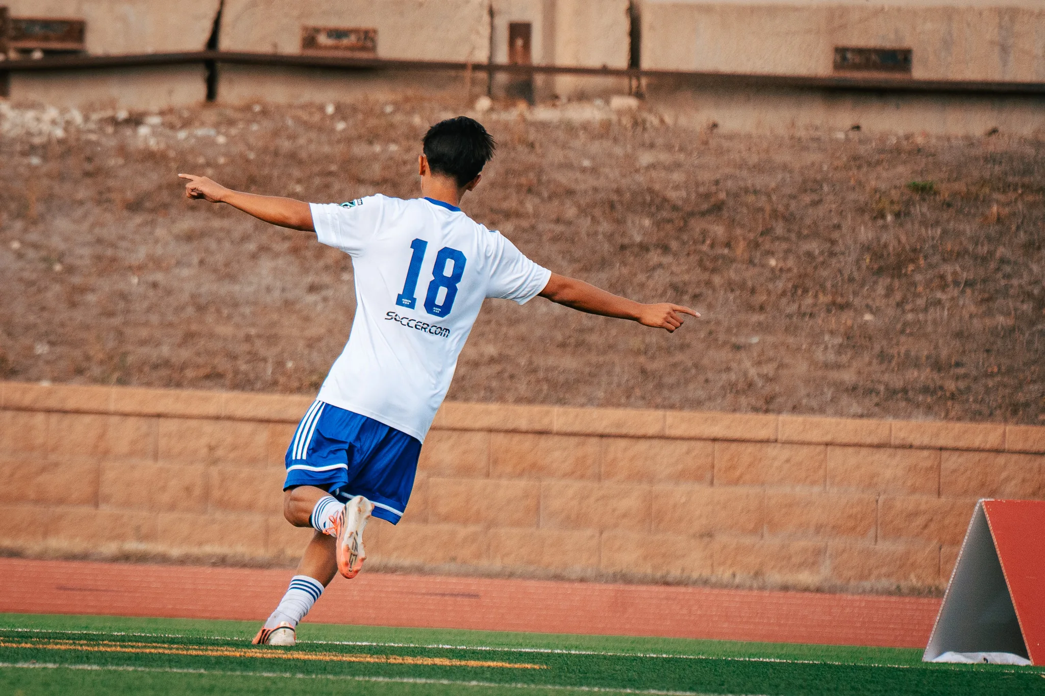 Seen from behind, Albion SC Colorado number 18 runs off with both arms spread wide