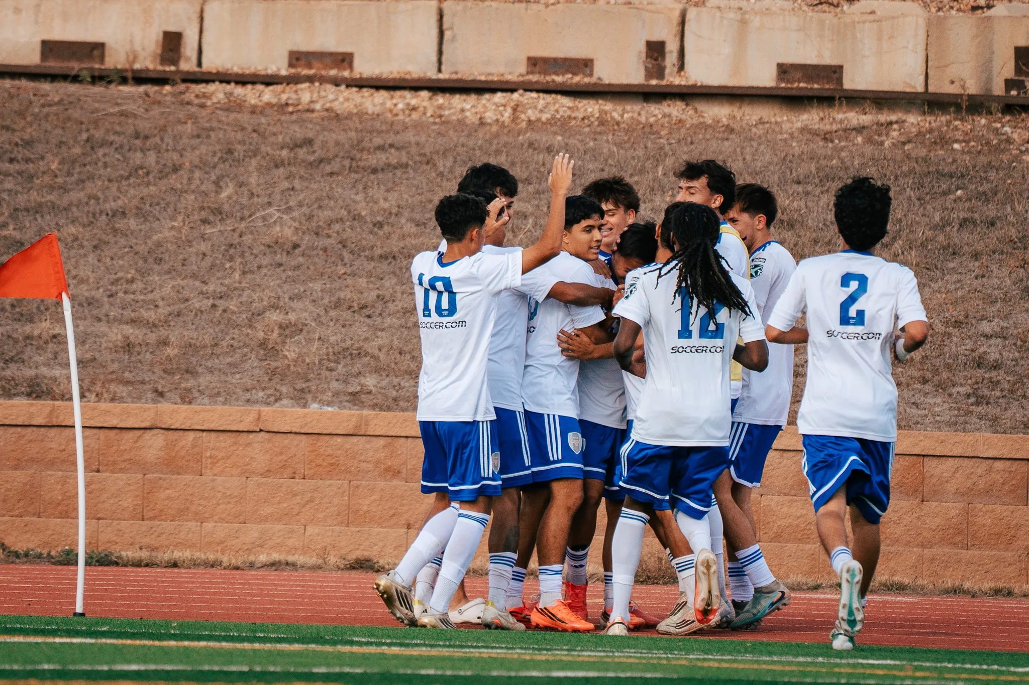 Albion SC Colorado players celebrate in a huddle by the corner flag, numbers 10, 12 and 2 among them