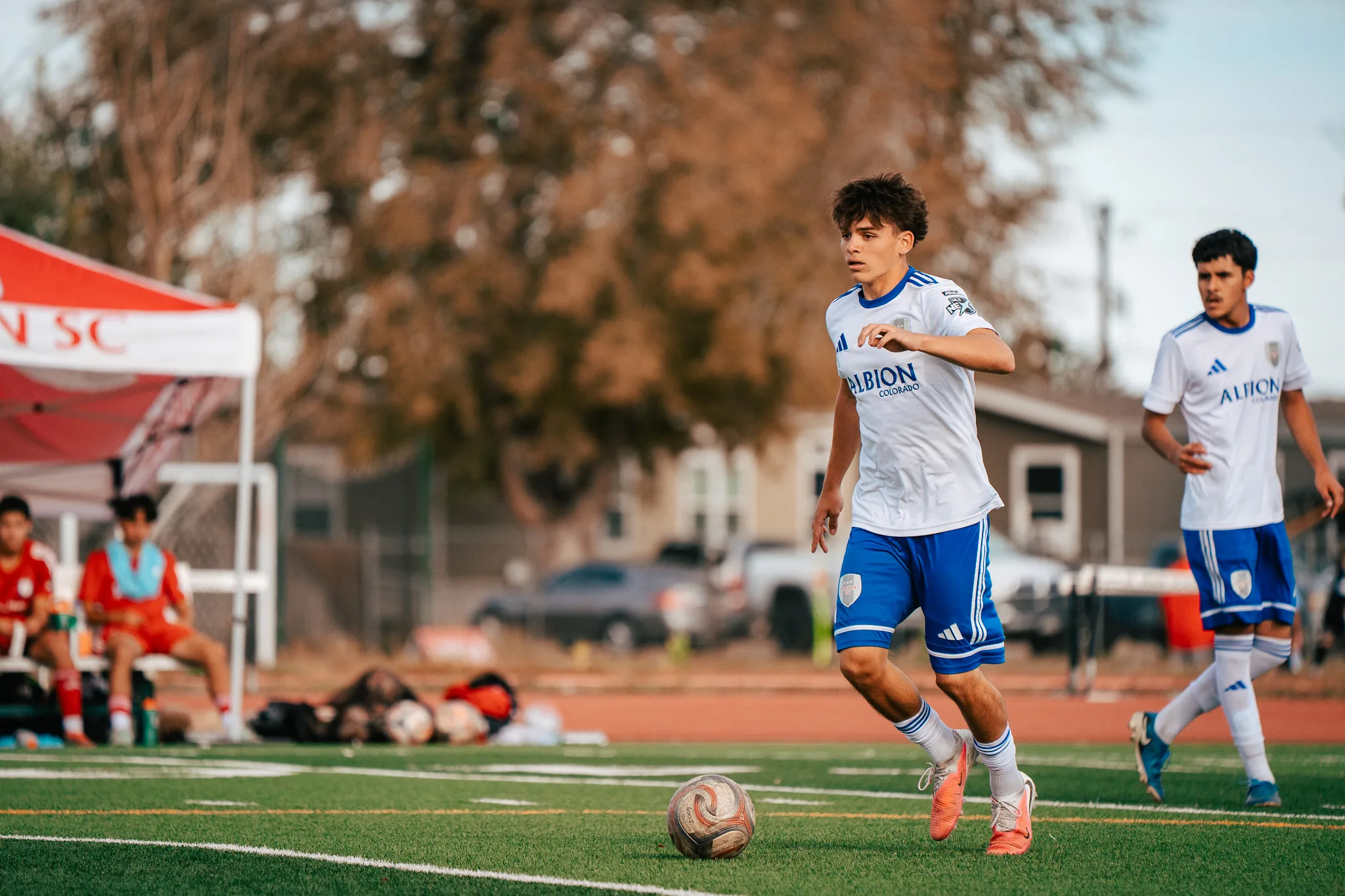 An Albion SC Colorado player brings the ball forward as a teammate trails him on the right