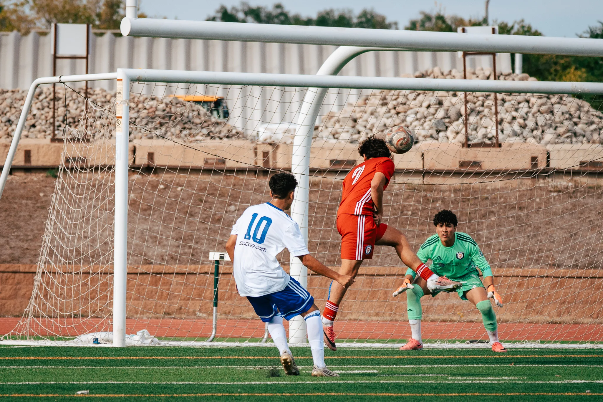 AC River number 9 heads the ball in front of the AC River goal as Albion SC Colorado number 10 closes in and the AC River goalkeeper in green crouches behind