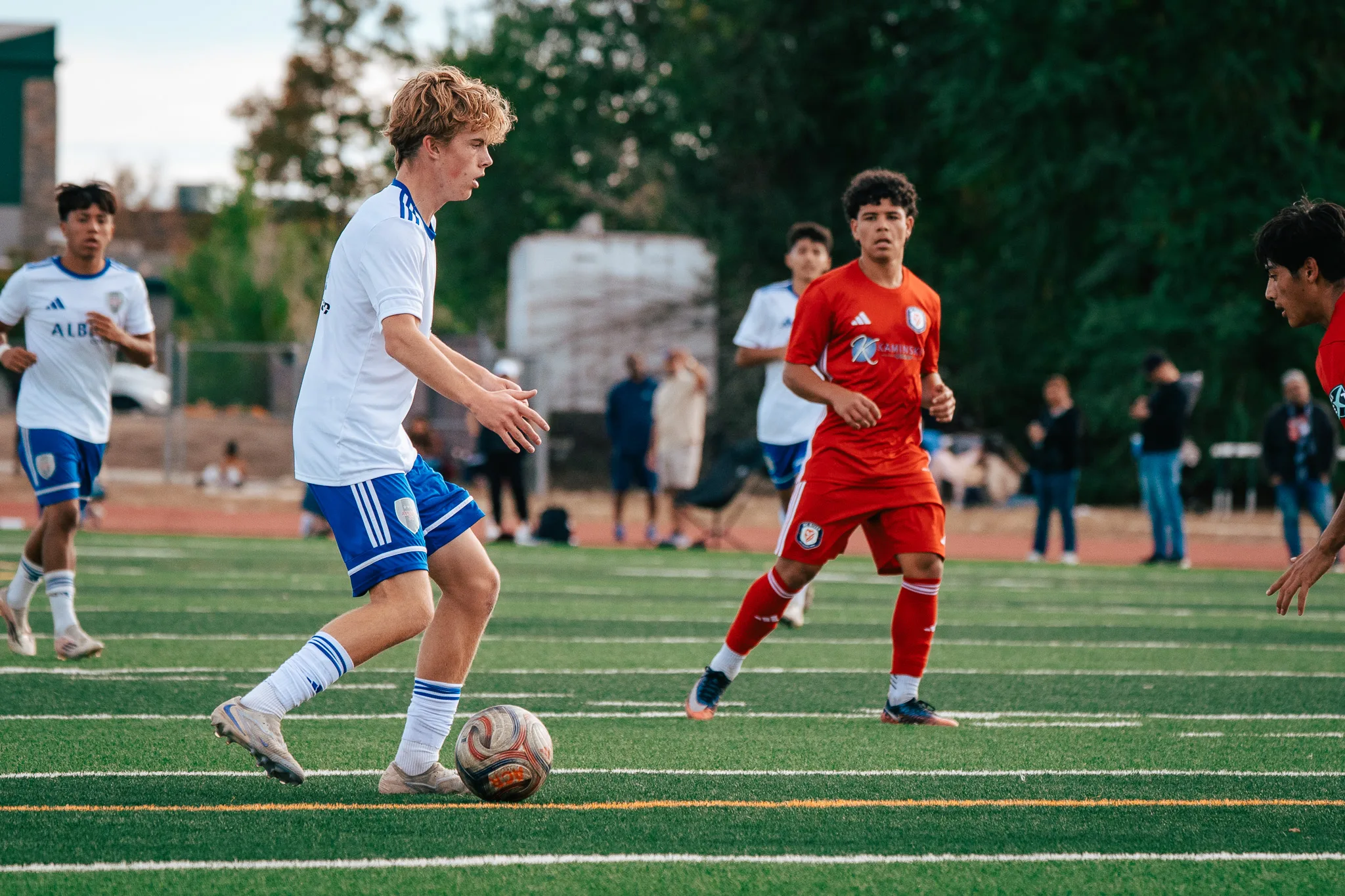 An Albion SC Colorado player with blond hair sets up a pass as an AC River player waits in front of him