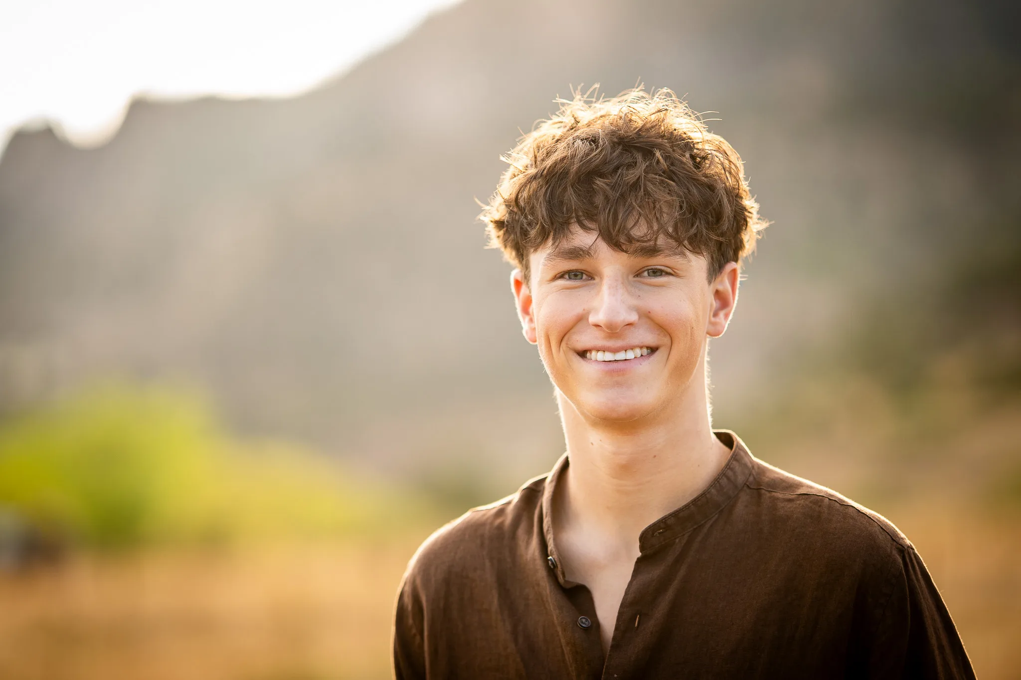 Arlo grins at the camera, backlit by warm evening light, a rocky ridge soft behind him.