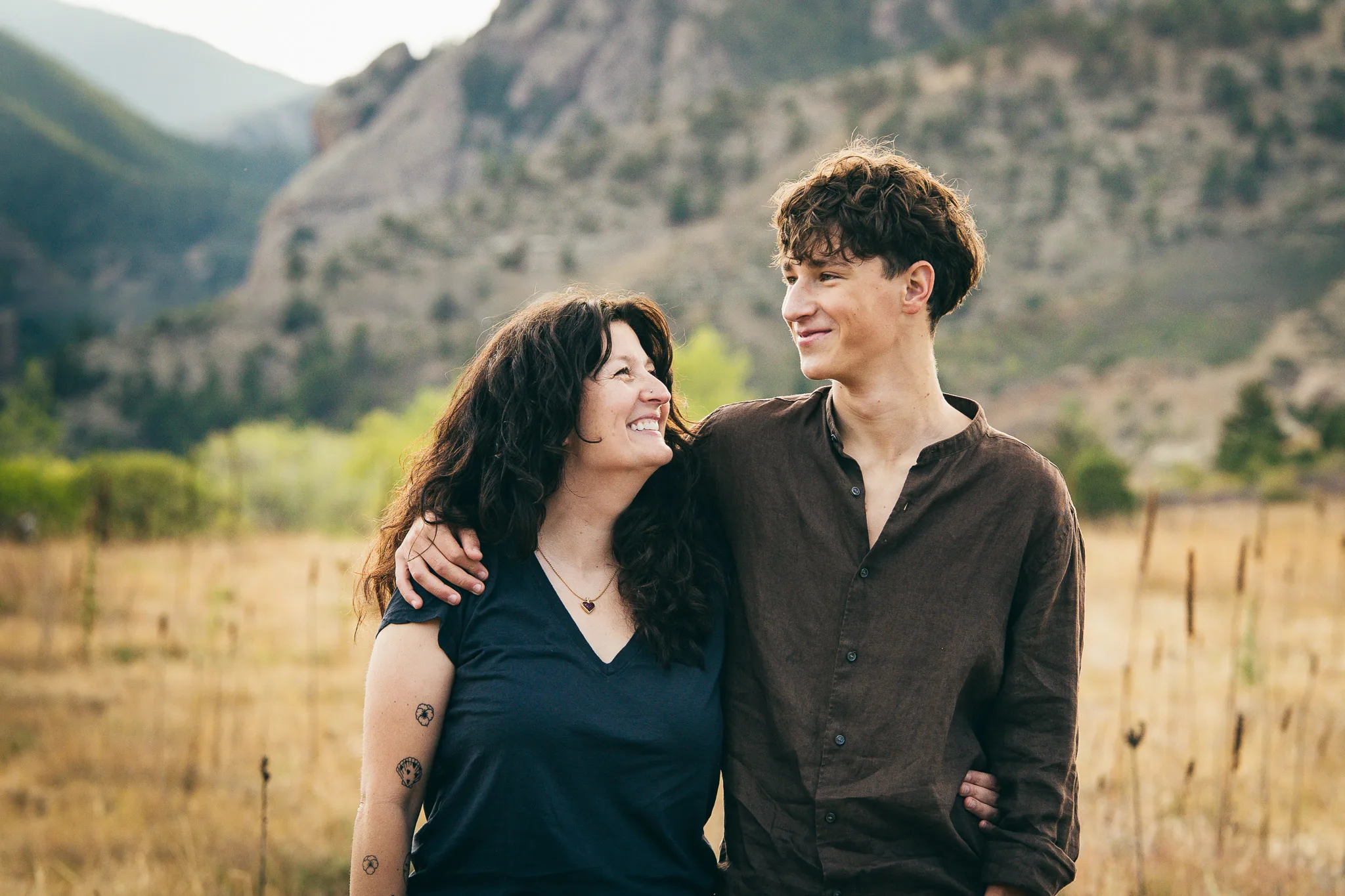 Arlo and his mom, Amy, smile at each other, arm in arm in a golden meadow below the foothills.