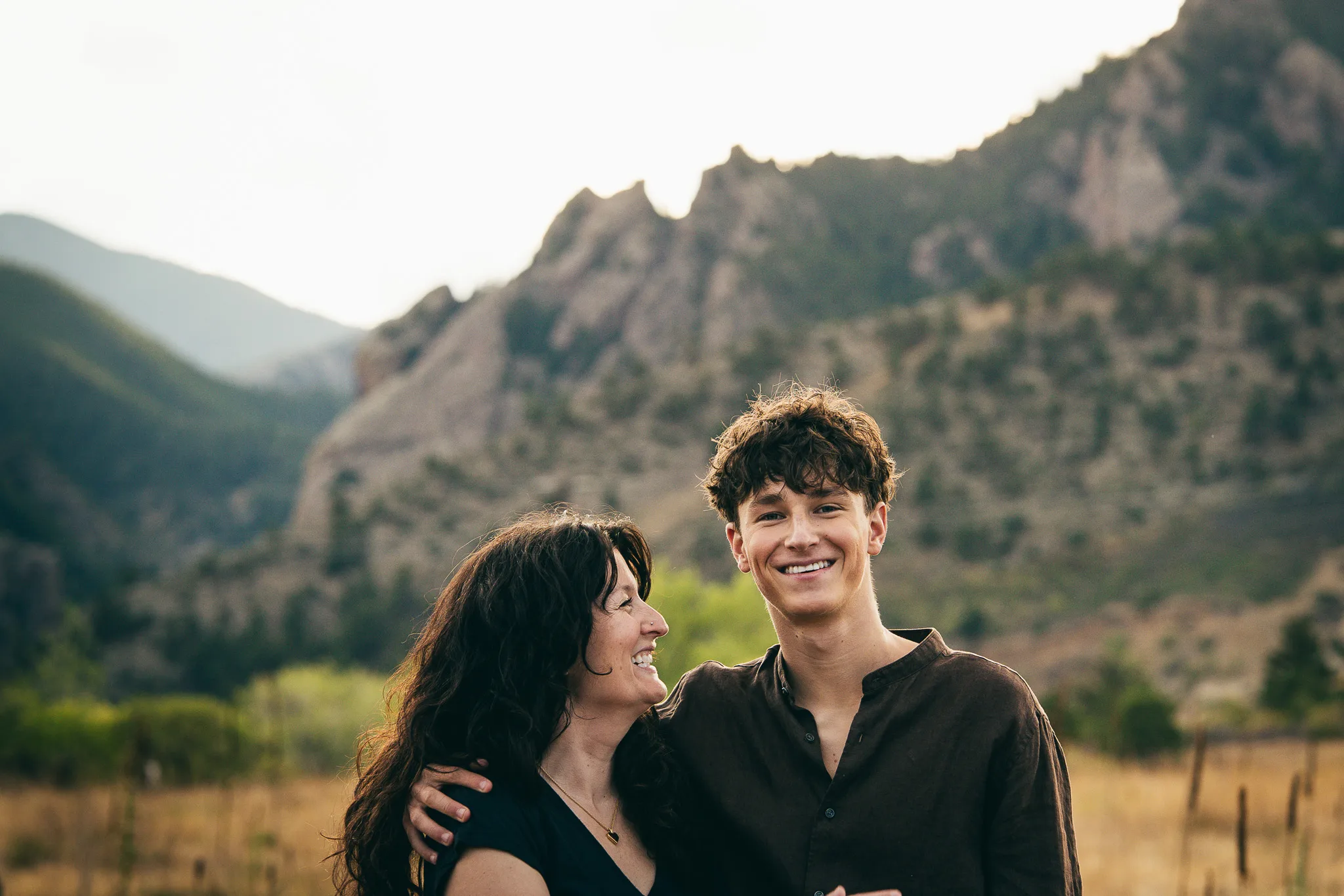 Arlo beams at the camera with an arm around his laughing mom, Amy, jagged foothills behind them.