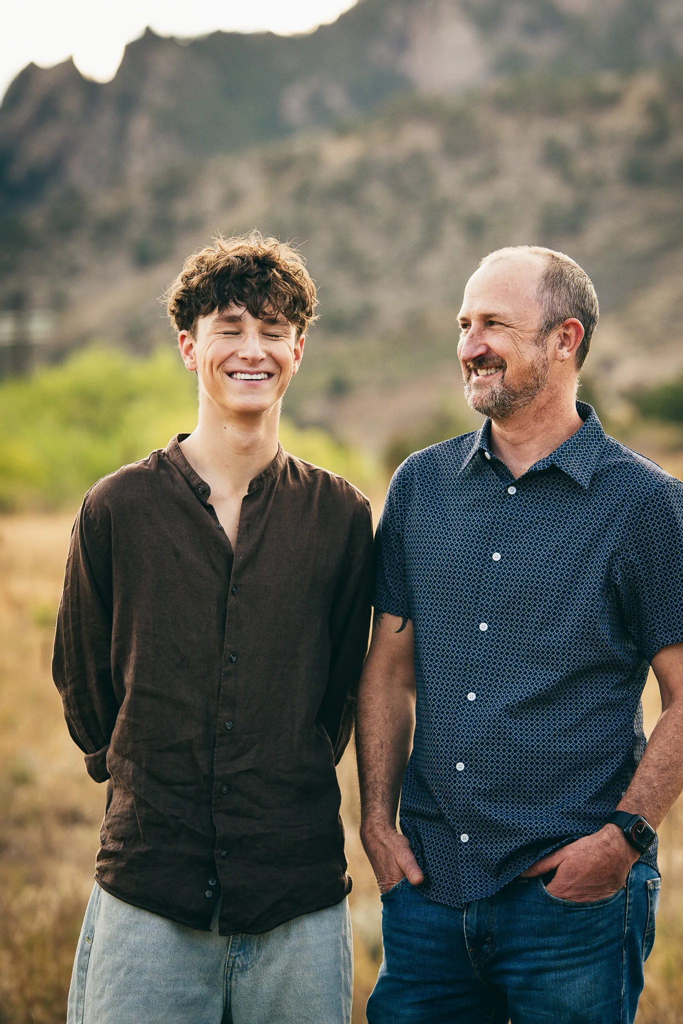 Arlo laughs with his eyes closed beside his smiling dad, Dusty, the foothills soft behind them.