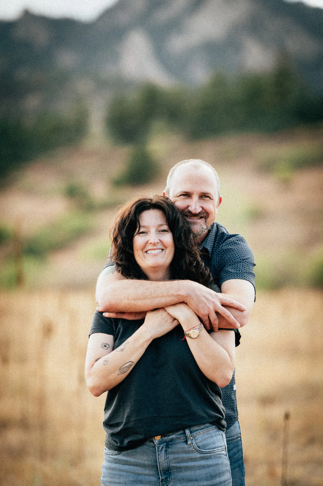 Arlo's parents, Amy and Dusty, share a hug in a golden field below the foothills.
