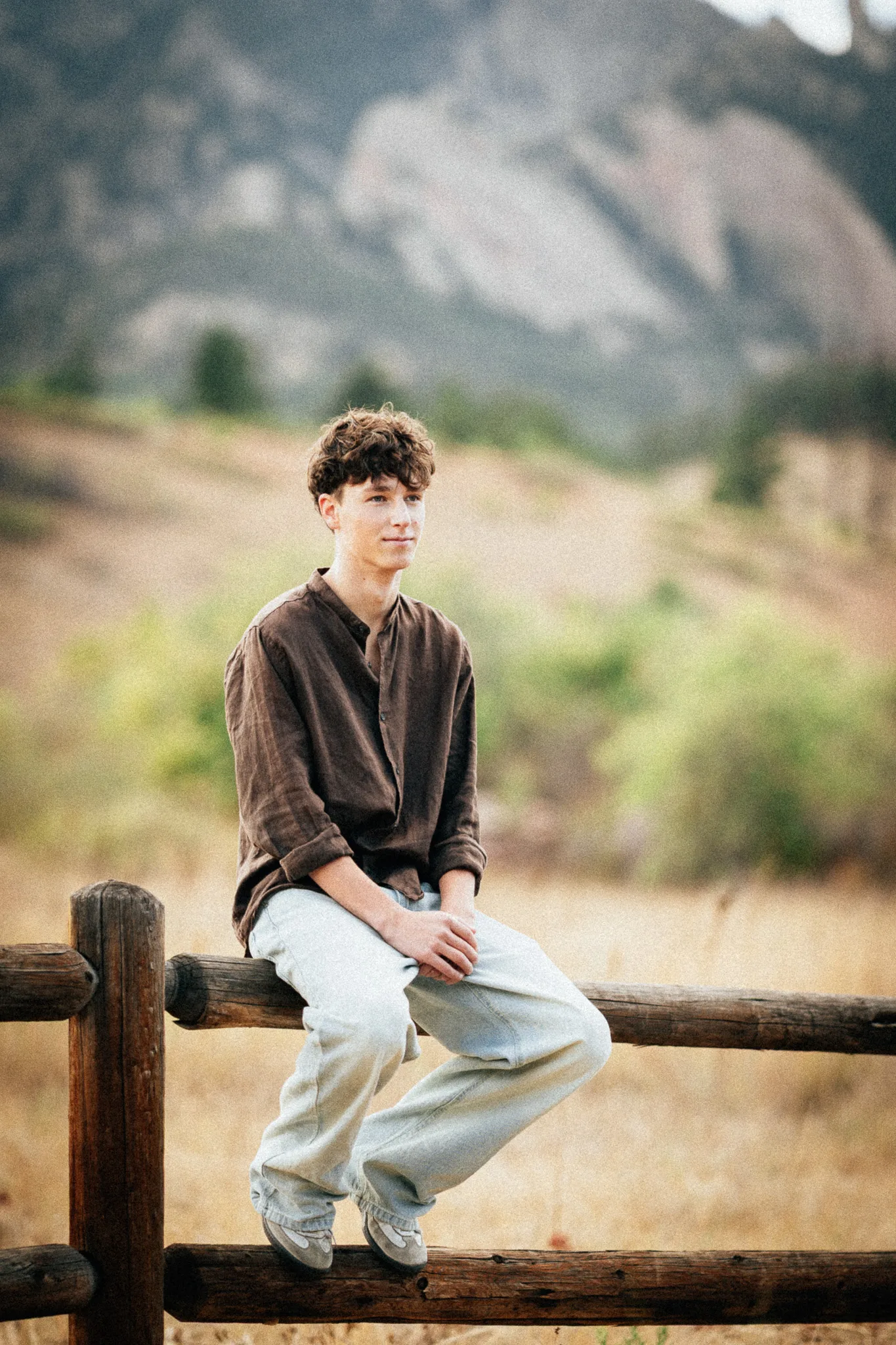 Arlo sits on a split-rail fence in a meadow, the pale rock of the Flatirons behind him.
