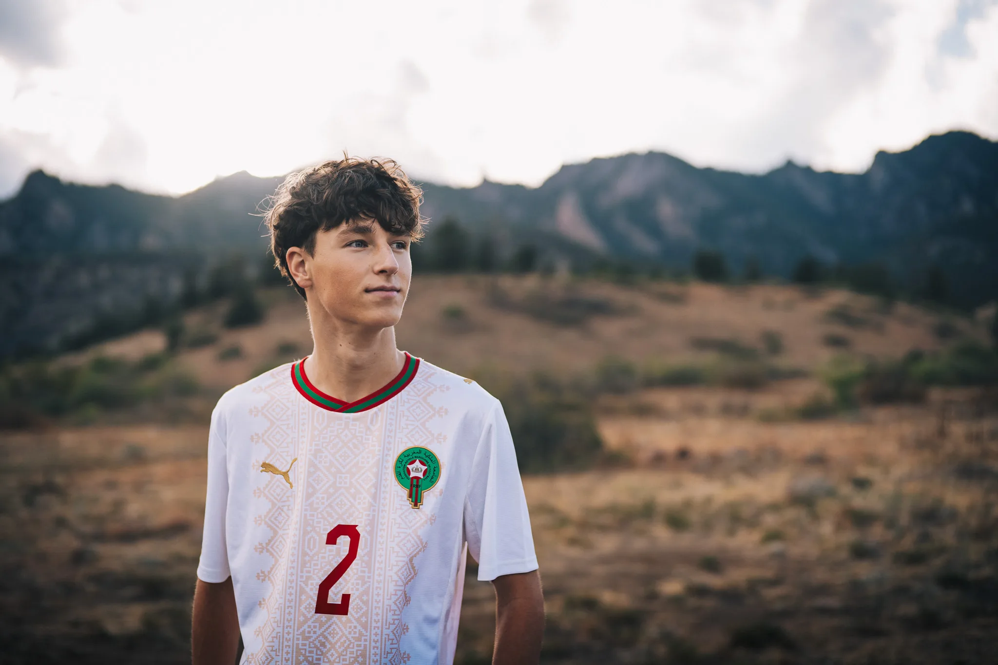 Arlo in a white number 2 soccer jersey, looking off to the side, the Flatirons behind him.