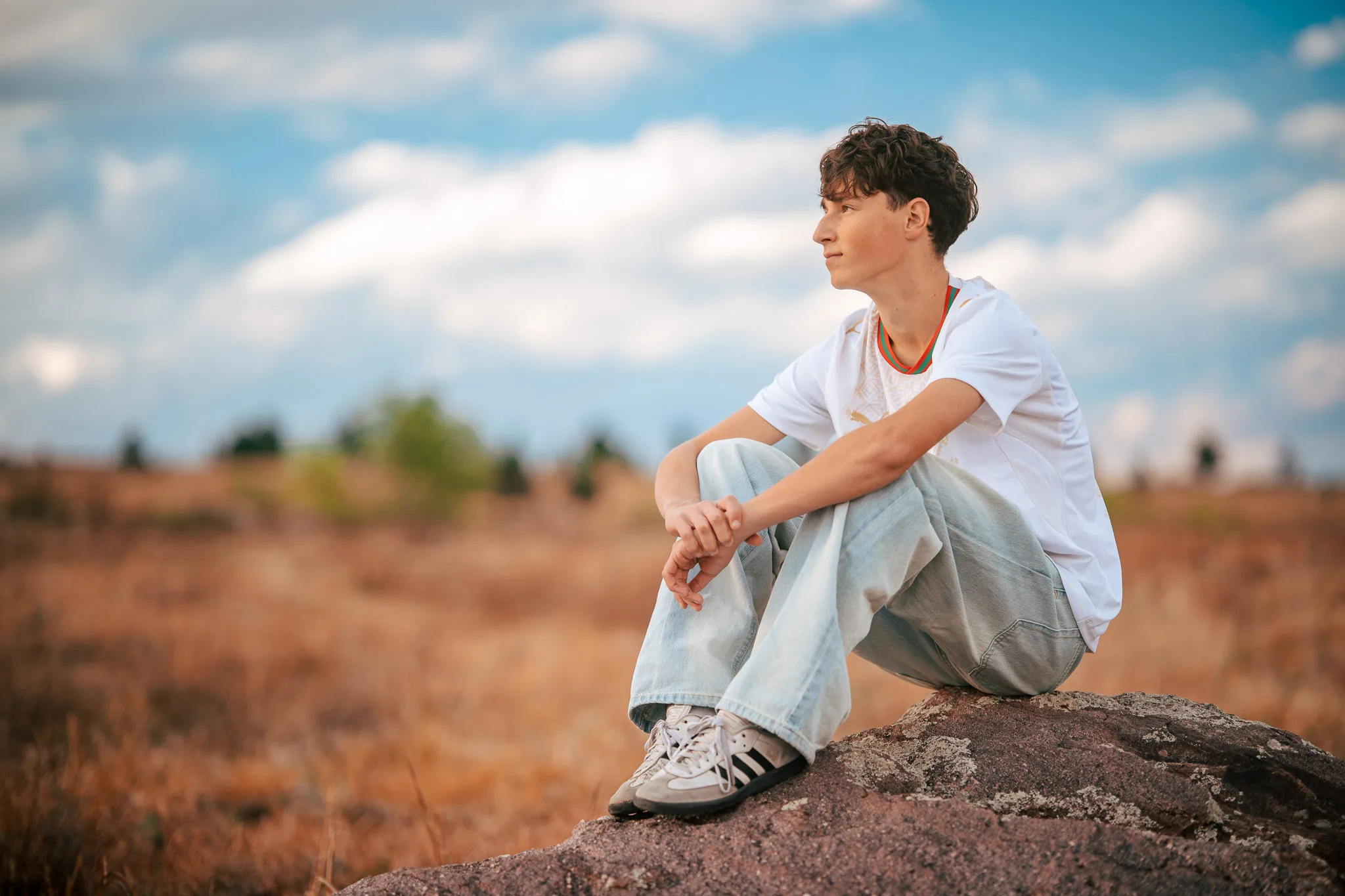 Arlo sits on a boulder, hands clasped over his knees, looking out across the dry grass.