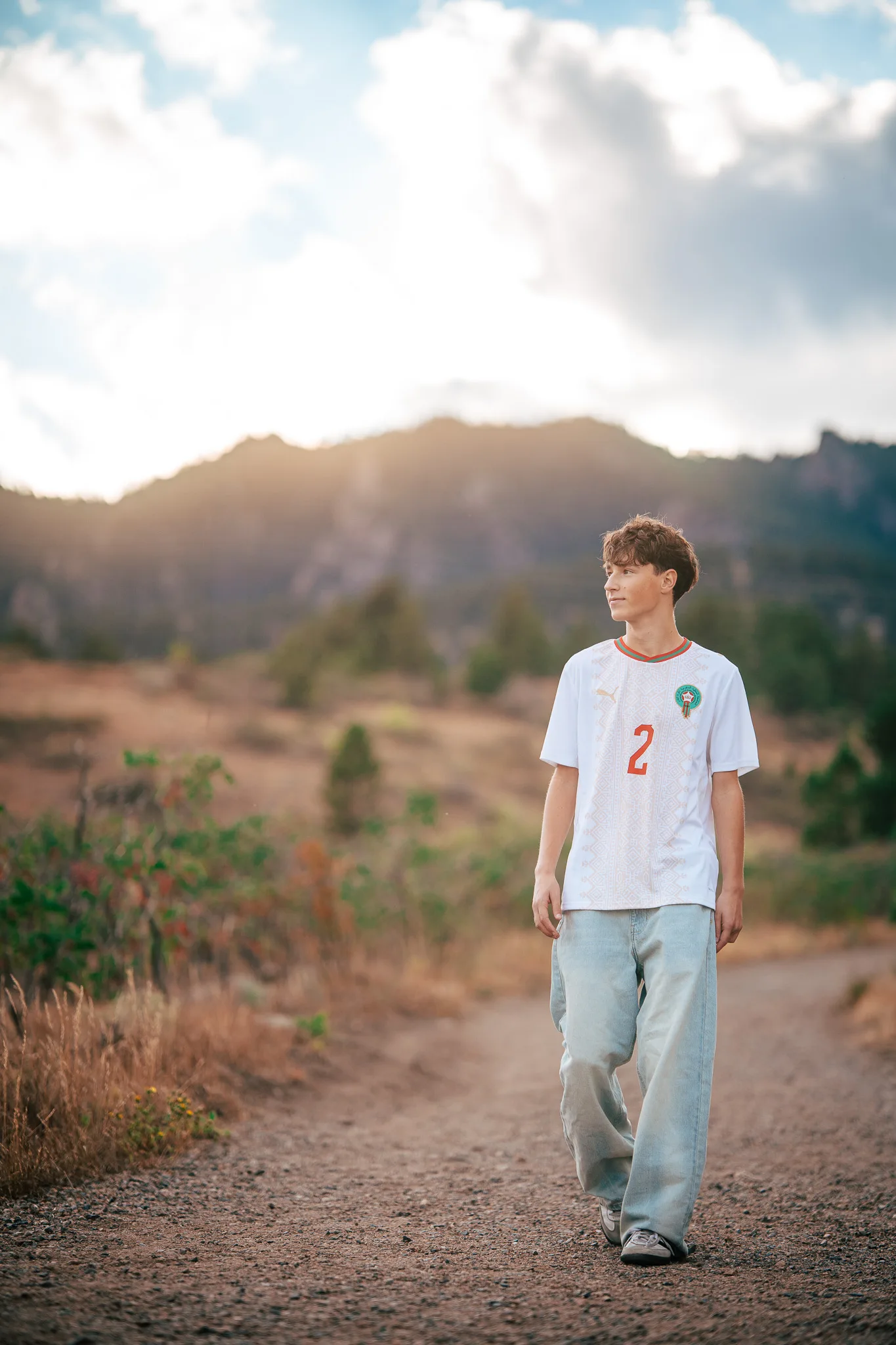 Arlo walks a dirt trail in a white number 2 soccer jersey as the sun sets over the foothills.