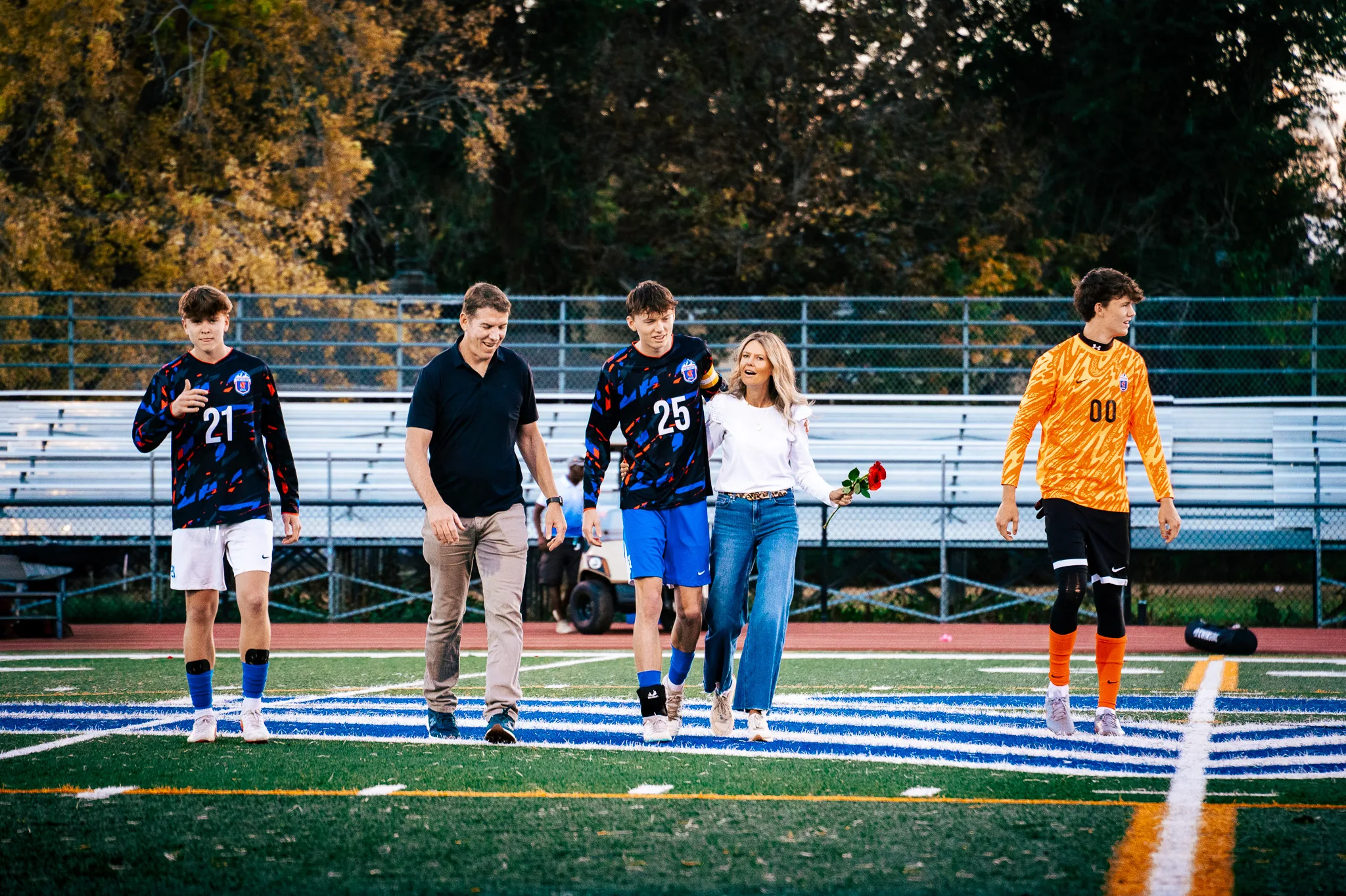 Centaurus number 25 walks onto the field arm in arm with a woman in white holding red roses, a man in a black polo beside them, number 21 on the left and the goalkeeper in orange, number 00, on the right