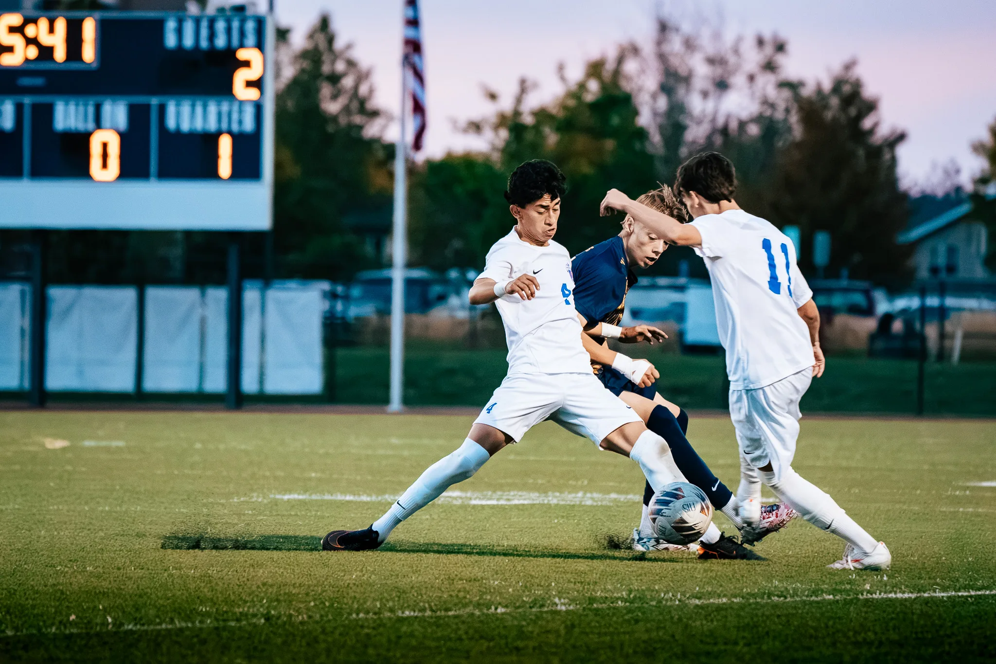 Centaurus number 4 stretches a leg for the ball against a Frederick player as Centaurus number 11 closes in from the right, the scoreboard behind them