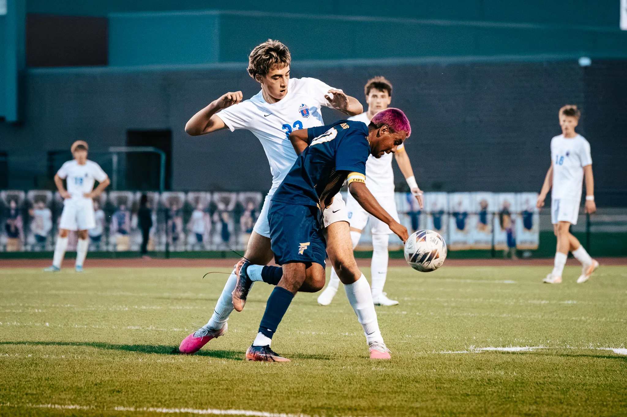 Centaurus number 23 leans over a Frederick player with pink hair as they fight for the ball, Centaurus players spread across the field behind them