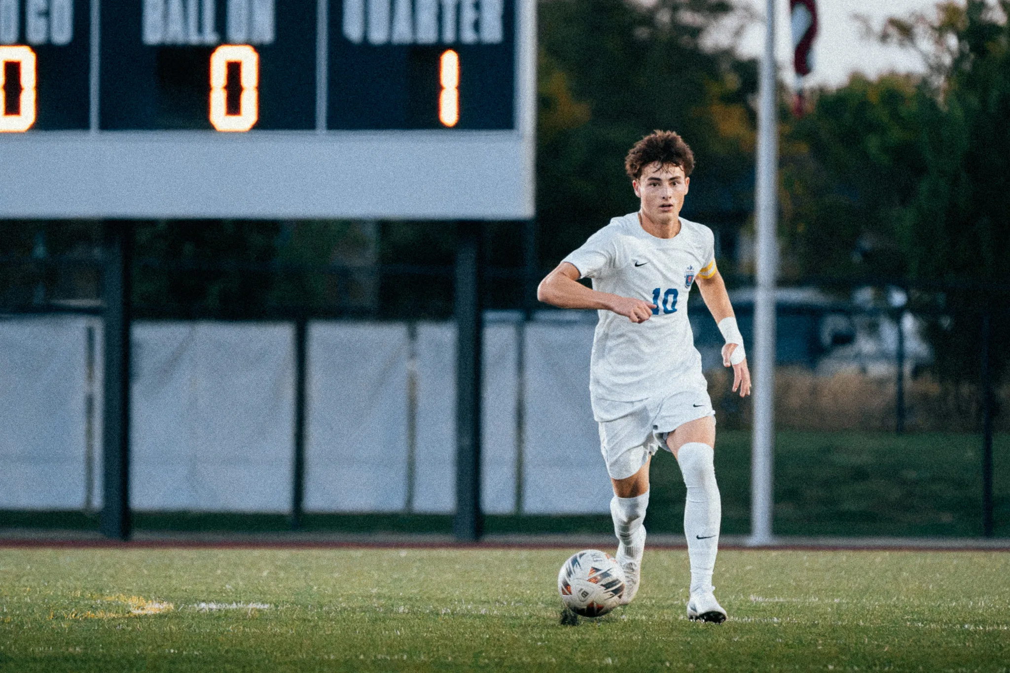 Centaurus number 10 dribbles the ball forward in the fading light, the scoreboard behind him