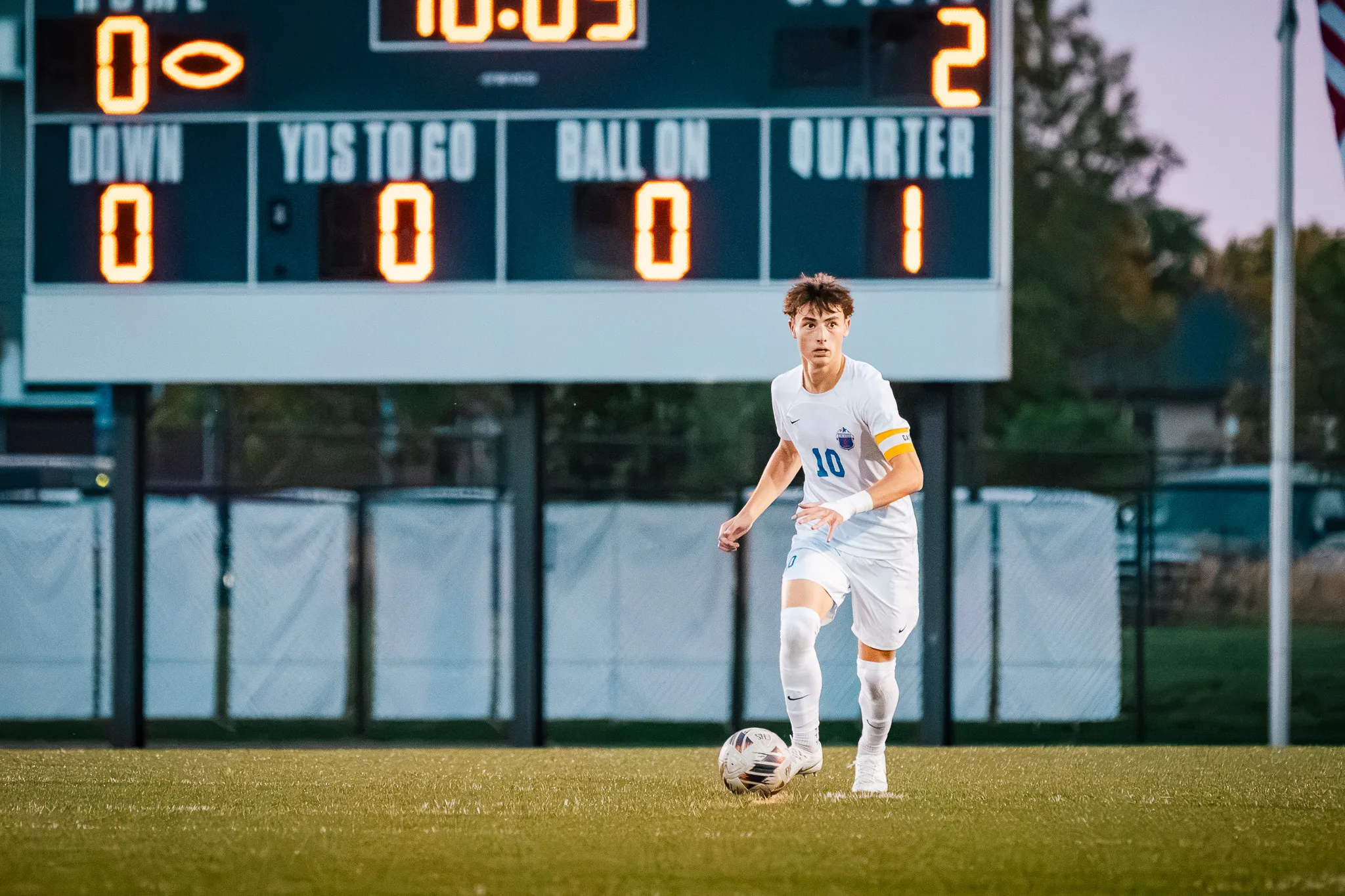 Looking ahead, Centaurus number 10 dribbles in open space beneath the scoreboard, the dusk sky pale behind him
