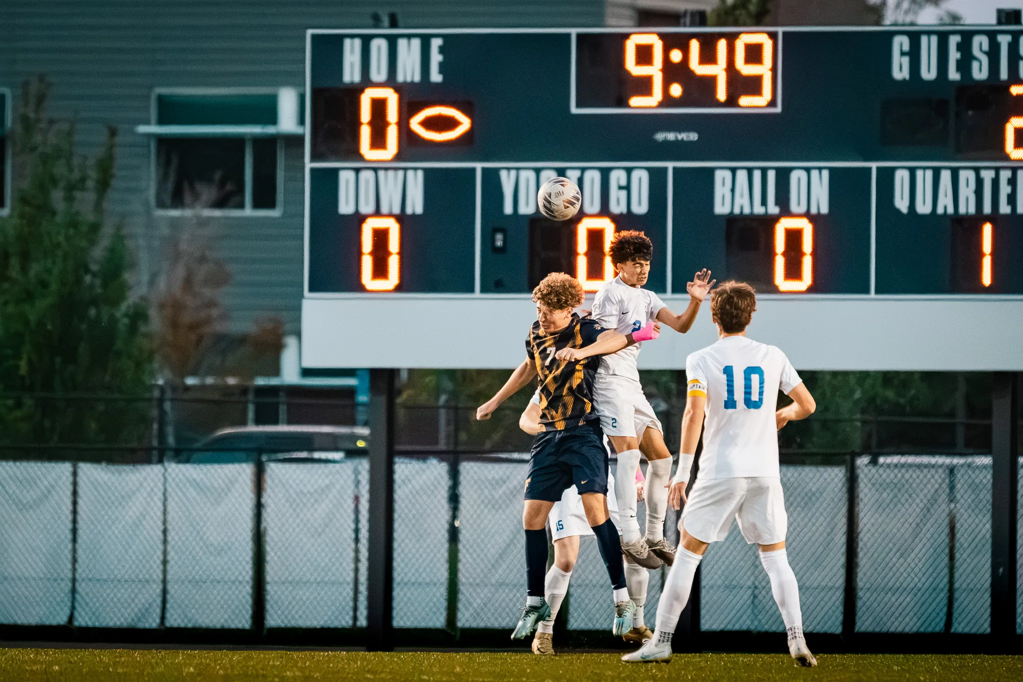 Under the scoreboard, a Frederick player and a Centaurus player rise together for a header as Centaurus number 10 watches