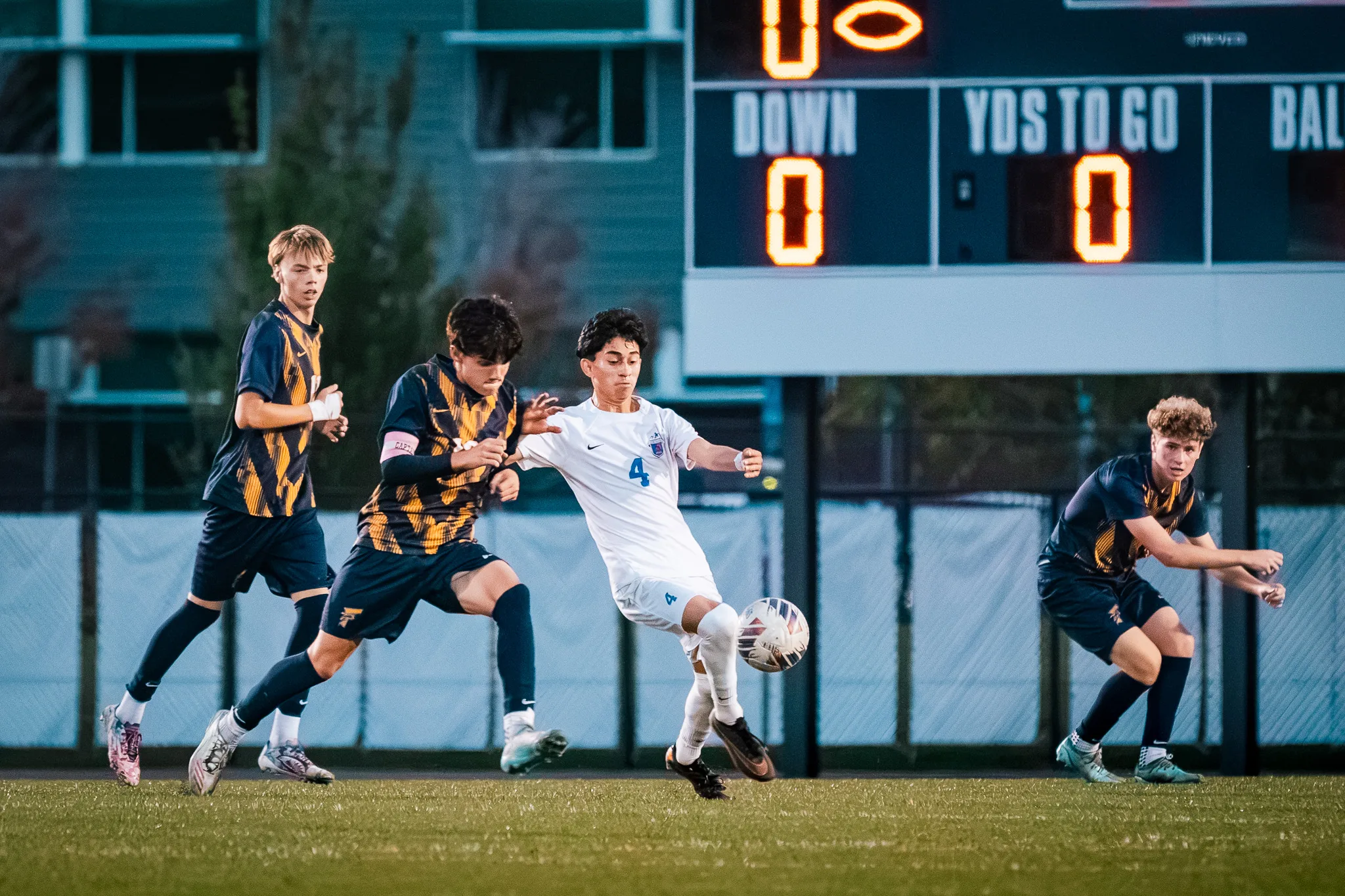 Centaurus number 4 plays the ball between two Frederick players as a third closes in from the right, the scoreboard above them
