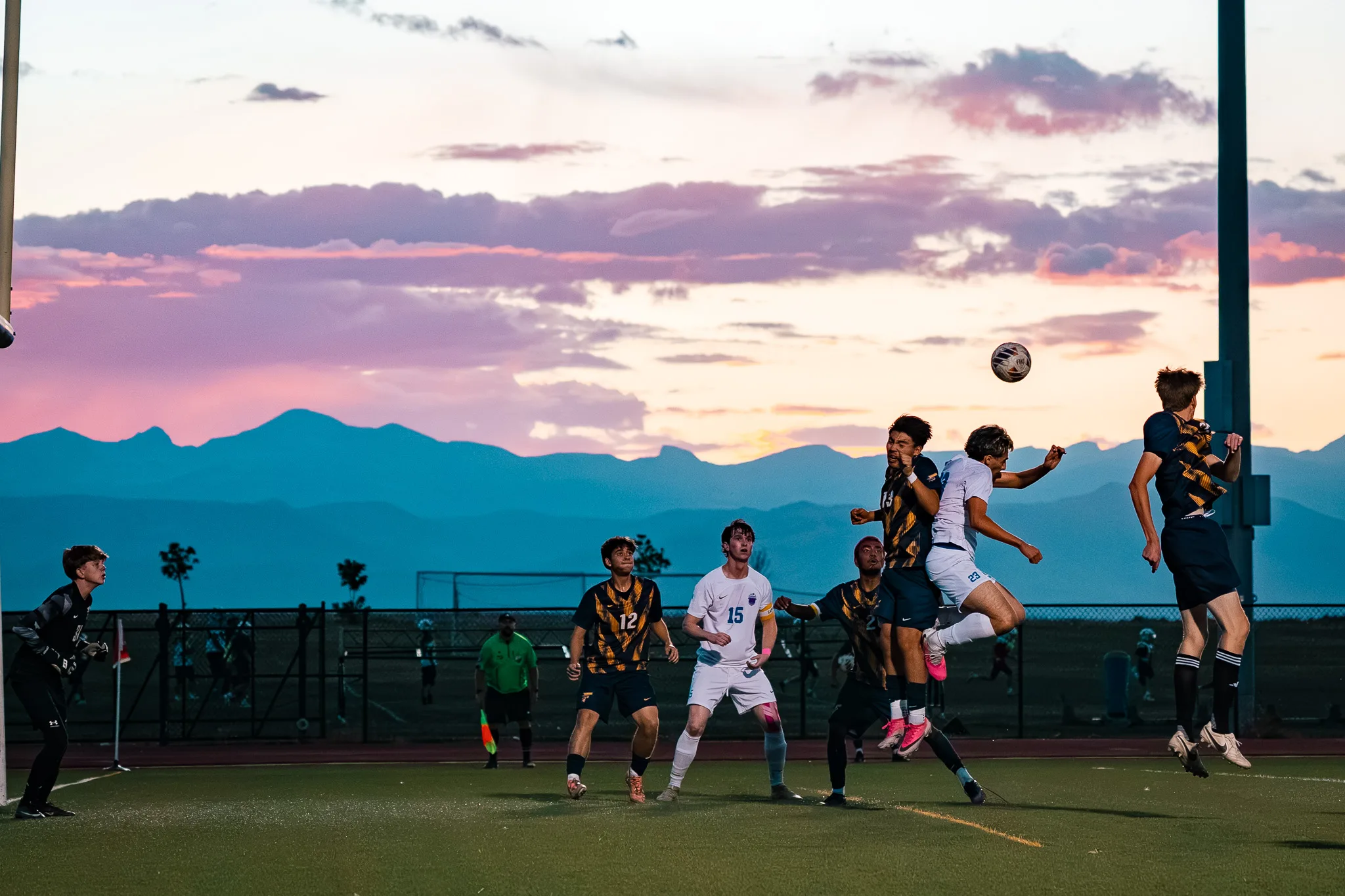 Beneath a purple and pink sunset, Centaurus number 23 and a Frederick player leap for a high ball near the goal as Centaurus number 15 and Frederick number 12 watch from below