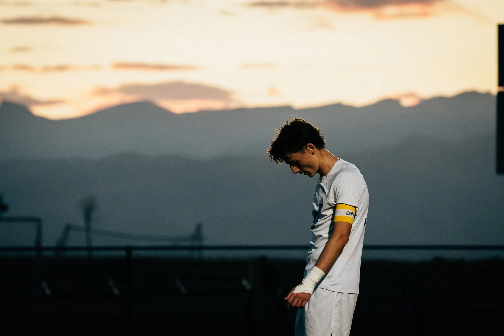 Against a pale sunset and the mountains, a Centaurus player wearing the captain's armband looks down with his head bowed
