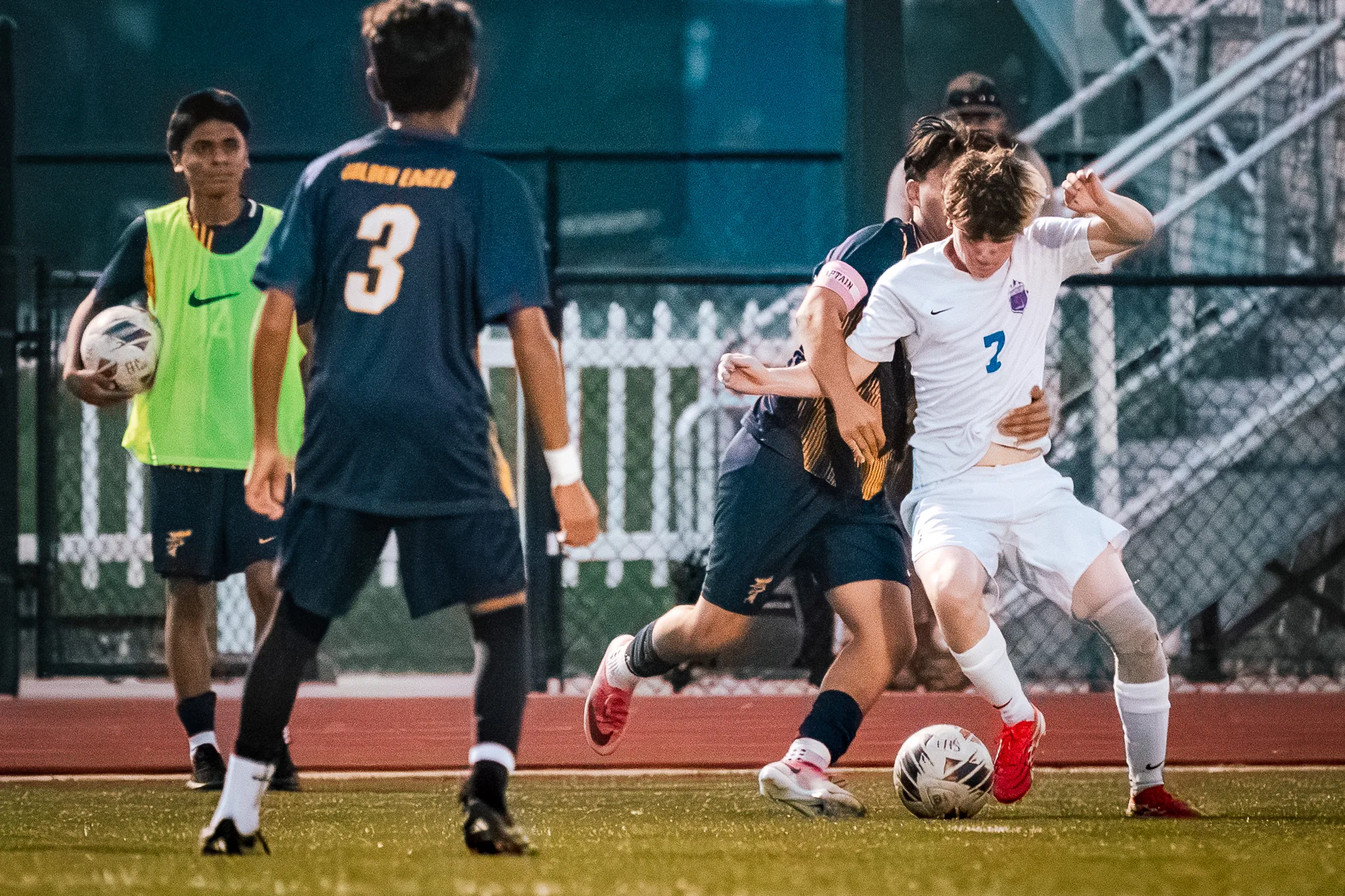 Centaurus number 7 and a Frederick player tangle for the ball near the sideline as Frederick number 3 watches and a substitute in a bright vest holds a ball behind him