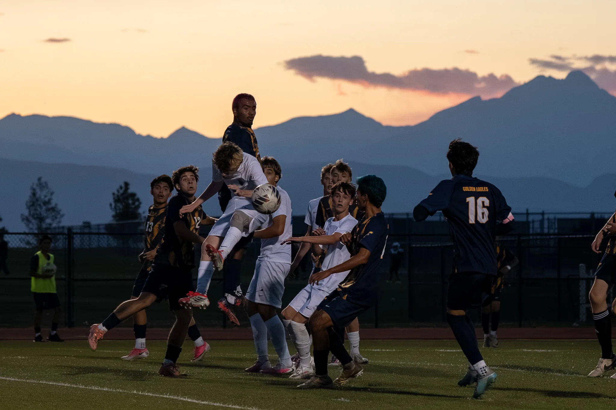 As the sky turns orange over the mountains, Centaurus and Frederick players crowd together in front of the goal for a ball in the air, Frederick number 16 standing apart at the right