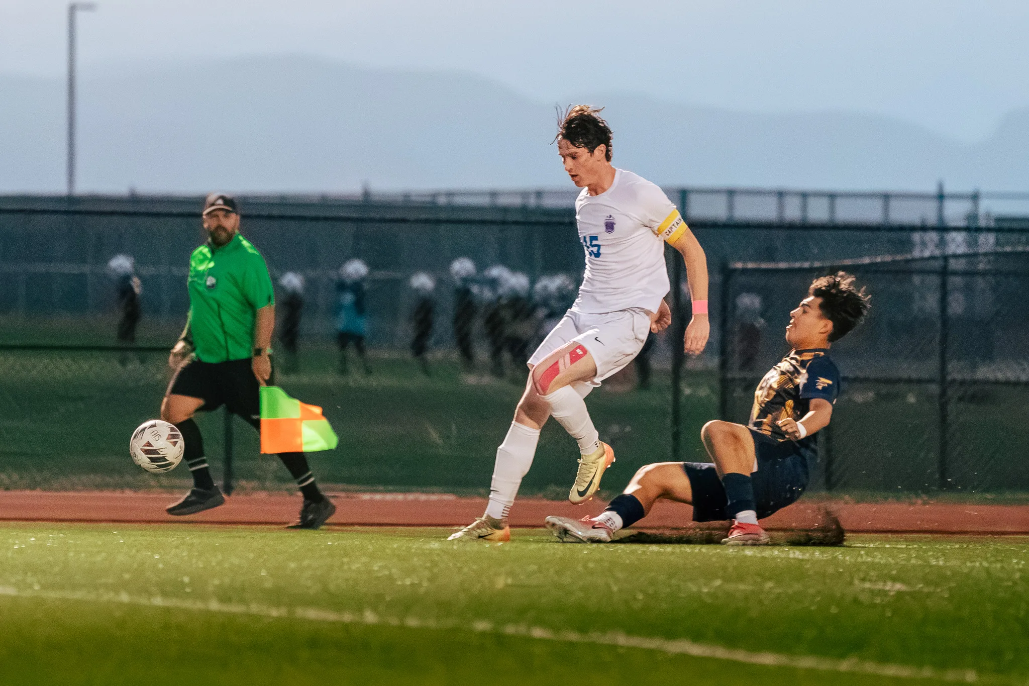 Centaurus number 15 jumps clear of a sliding Frederick player as the ball rolls toward an assistant referee in green on the sideline