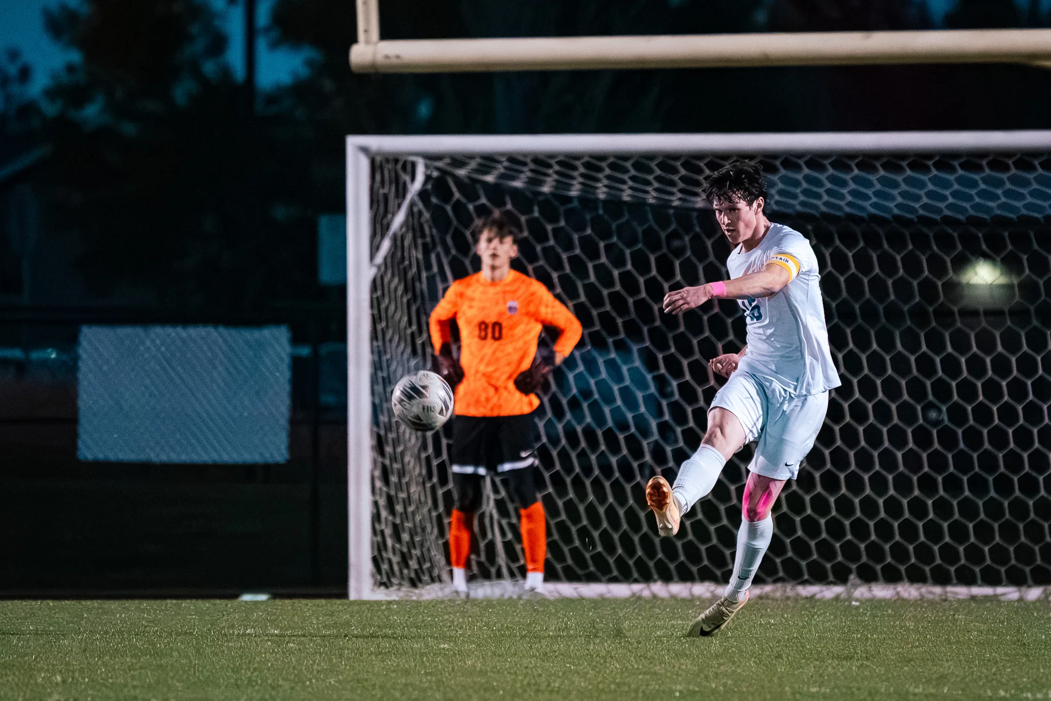 In front of the goal, a Centaurus player in a yellow armband boots the ball away as the goalkeeper in orange, number 00, watches behind him
