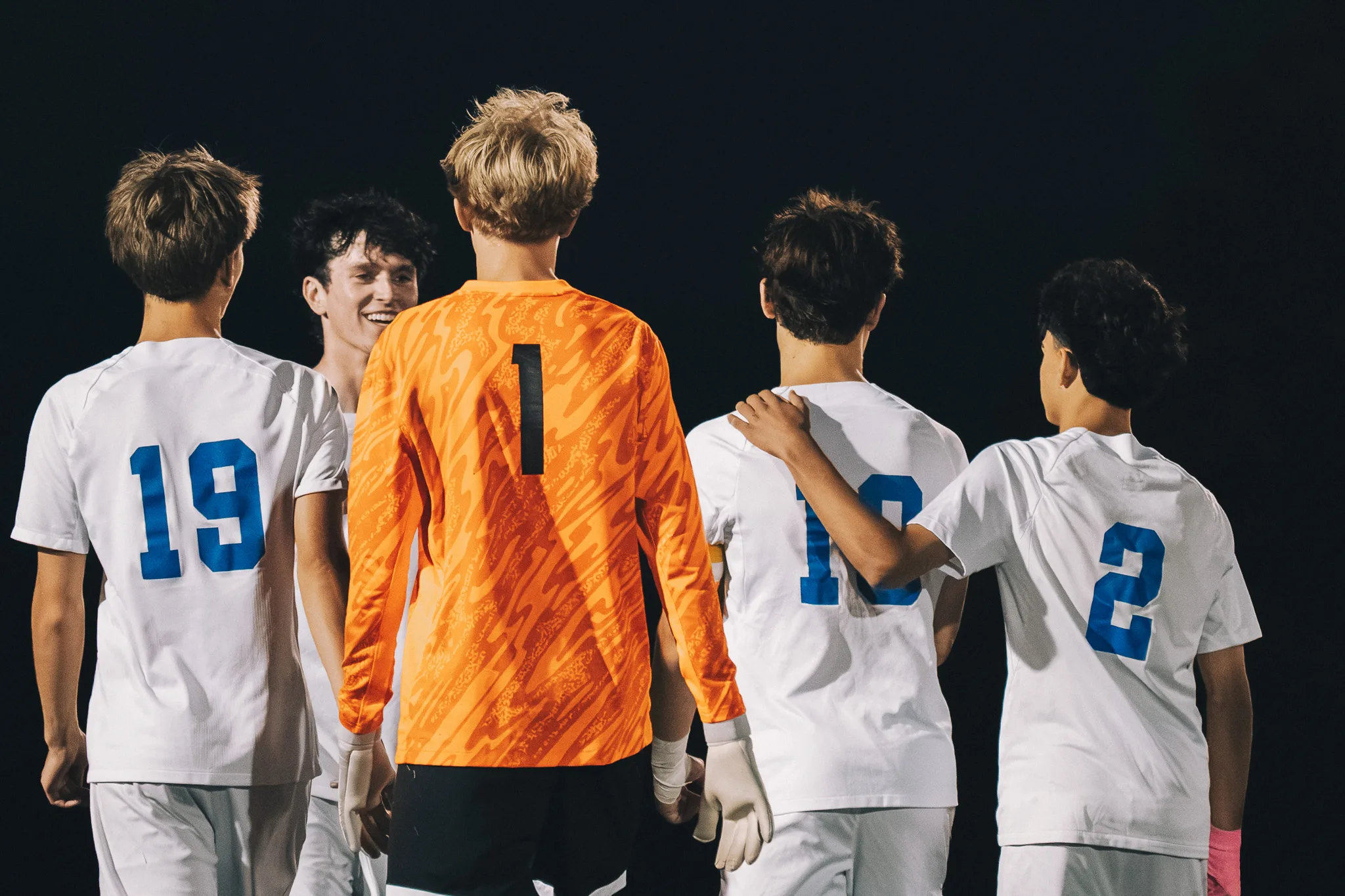 Against the night, the Centaurus goalkeeper in orange, number 1, walks with teammates including numbers 19 and 2, one of them smiling