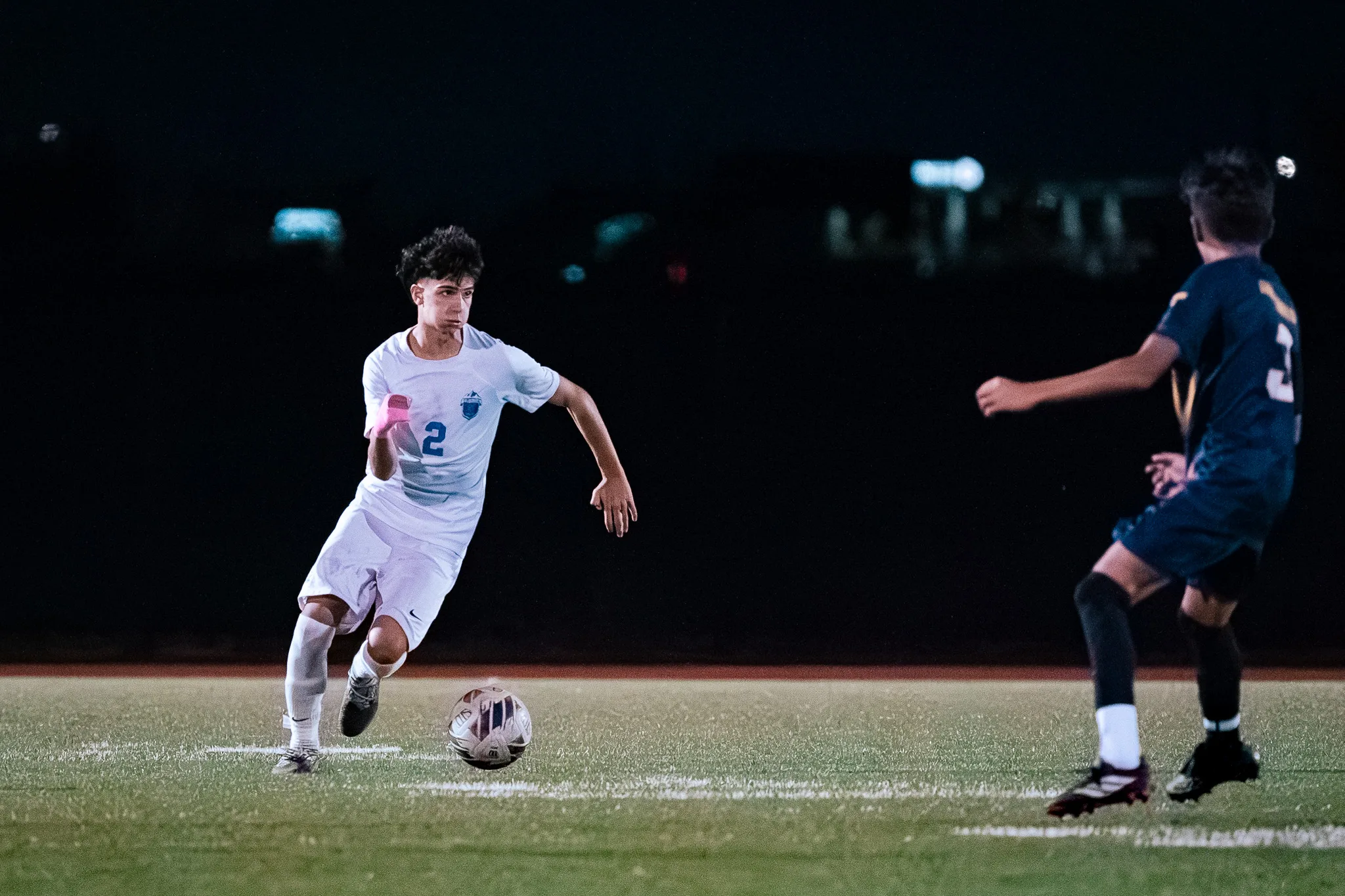 Centaurus number 2 dribbles the ball at night, his eyes on a Frederick player approaching from the right