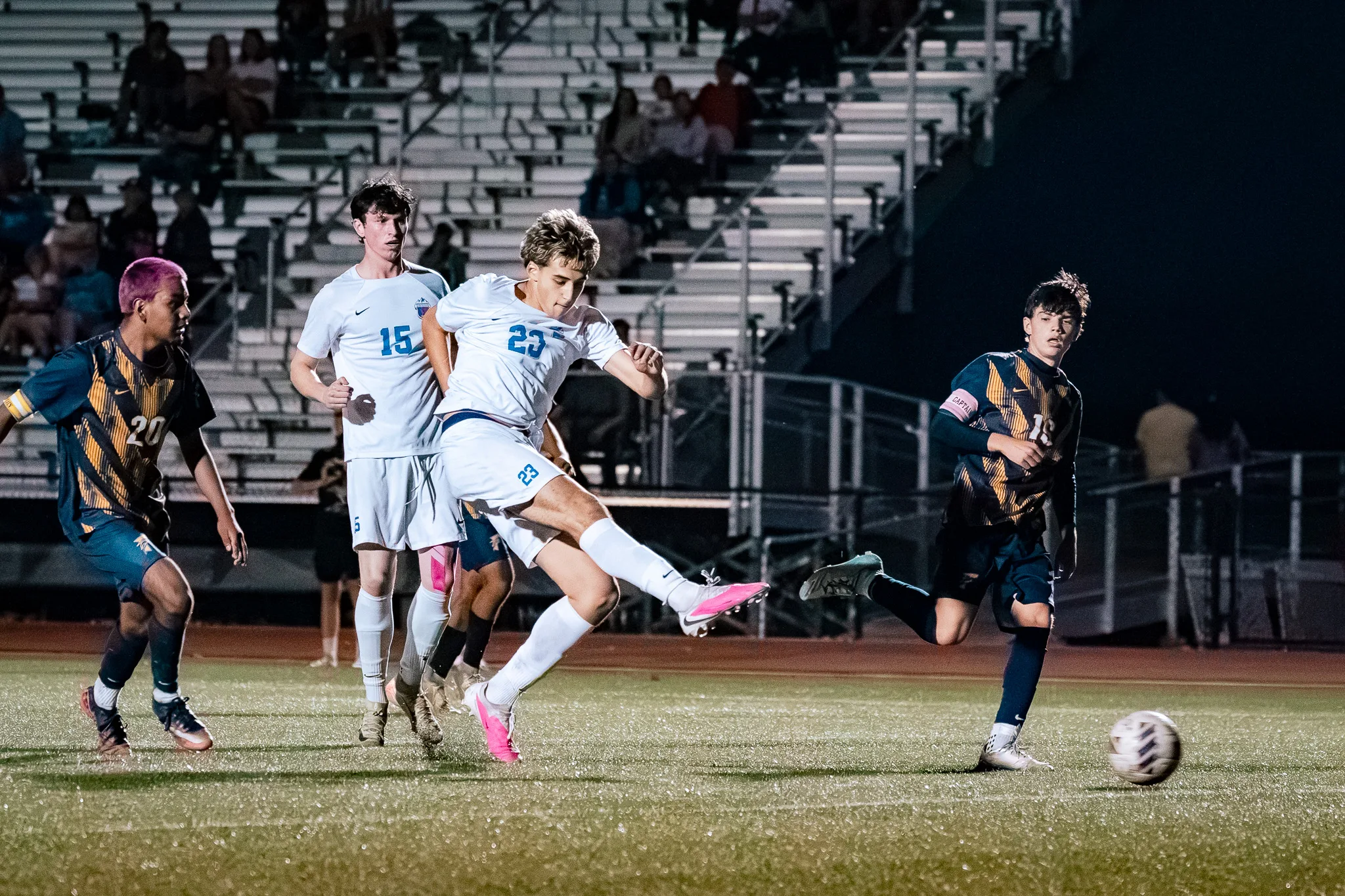 Centaurus number 23 swings his leg through the ball in pink cleats as Centaurus number 15 stands behind him and Frederick number 20 and another Frederick player look on