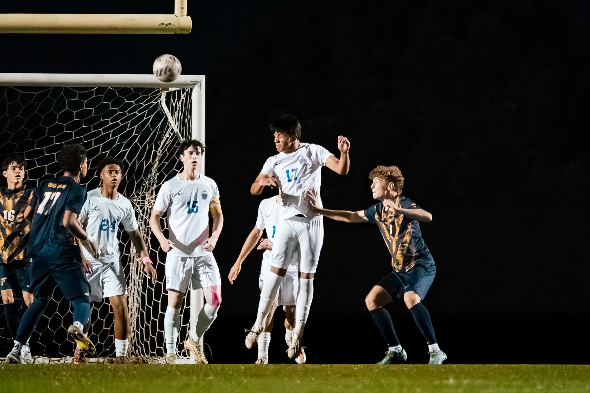 Under the lights in front of the goal, Centaurus number 17 leaps for a high ball with numbers 15 and 24 beside him and Frederick players crowding in