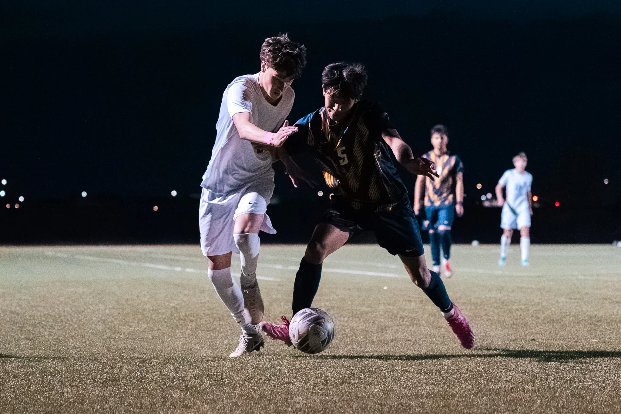 Shoulder to shoulder at night, a Centaurus player and Frederick number 5 fight for the ball, two more players in the distance