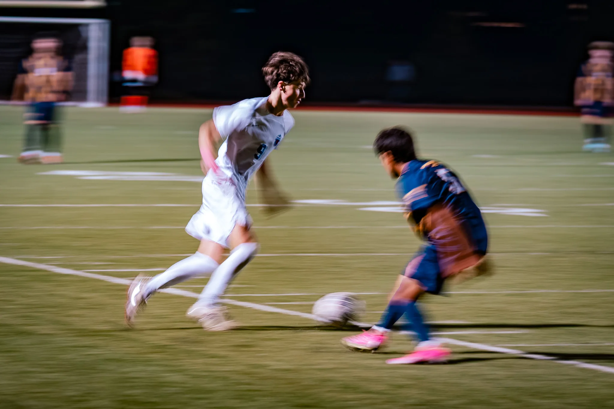 In a panning blur, Centaurus number 9 runs with the ball while a Frederick player in pink cleats crouches to meet him