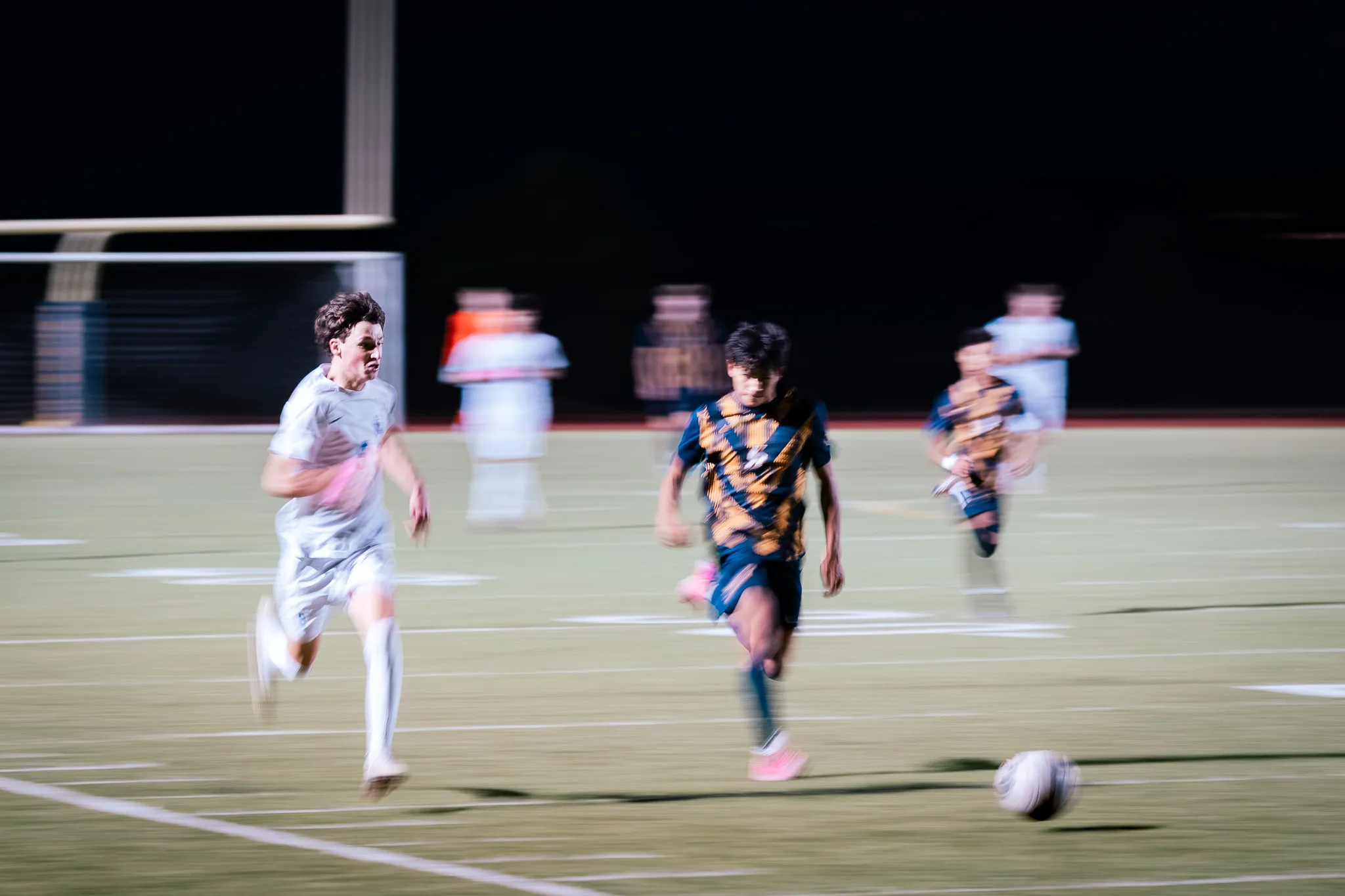 In a streak of motion, a Centaurus player and a Frederick player in pink cleats race side by side after the ball, the goal blurred behind them