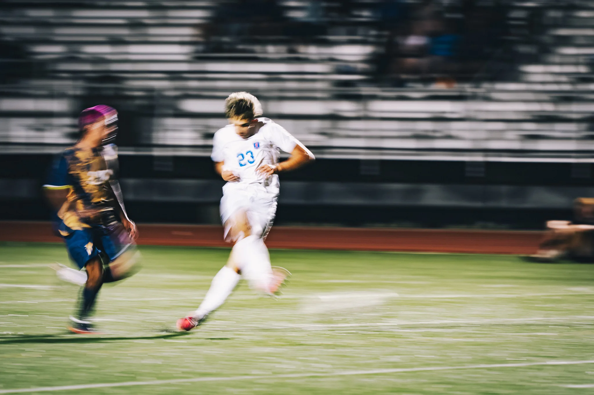 Centaurus number 23 runs through the frame in a panning blur, a Frederick player streaking beside him, the bleachers smeared behind
