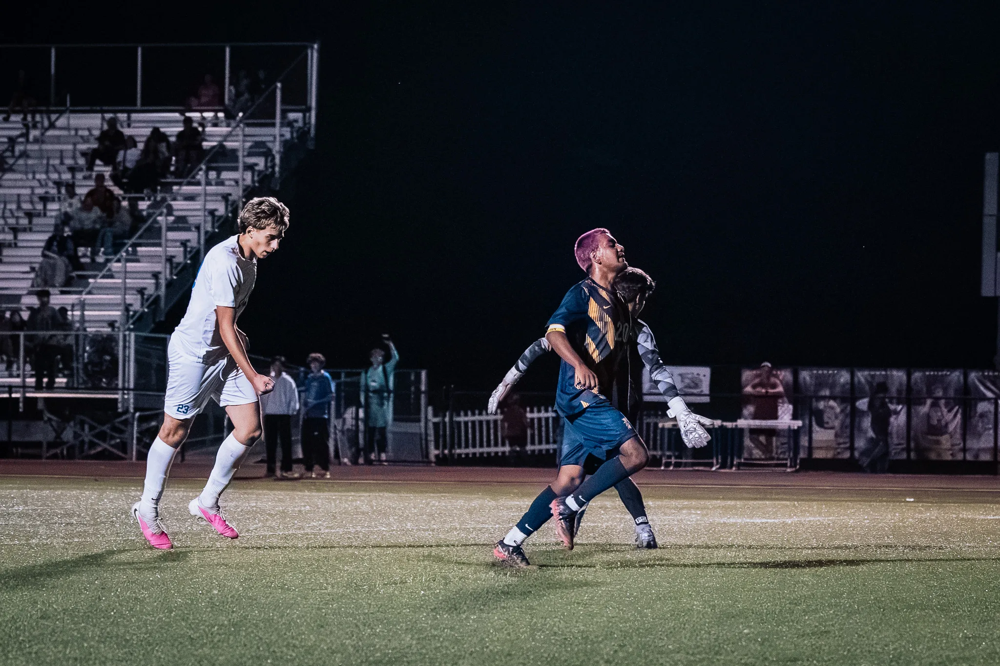 Centaurus number 23 in pink cleats looks on from the left while Frederick number 20 and a goalkeeper in white gloves stand together at the right, the bleachers behind