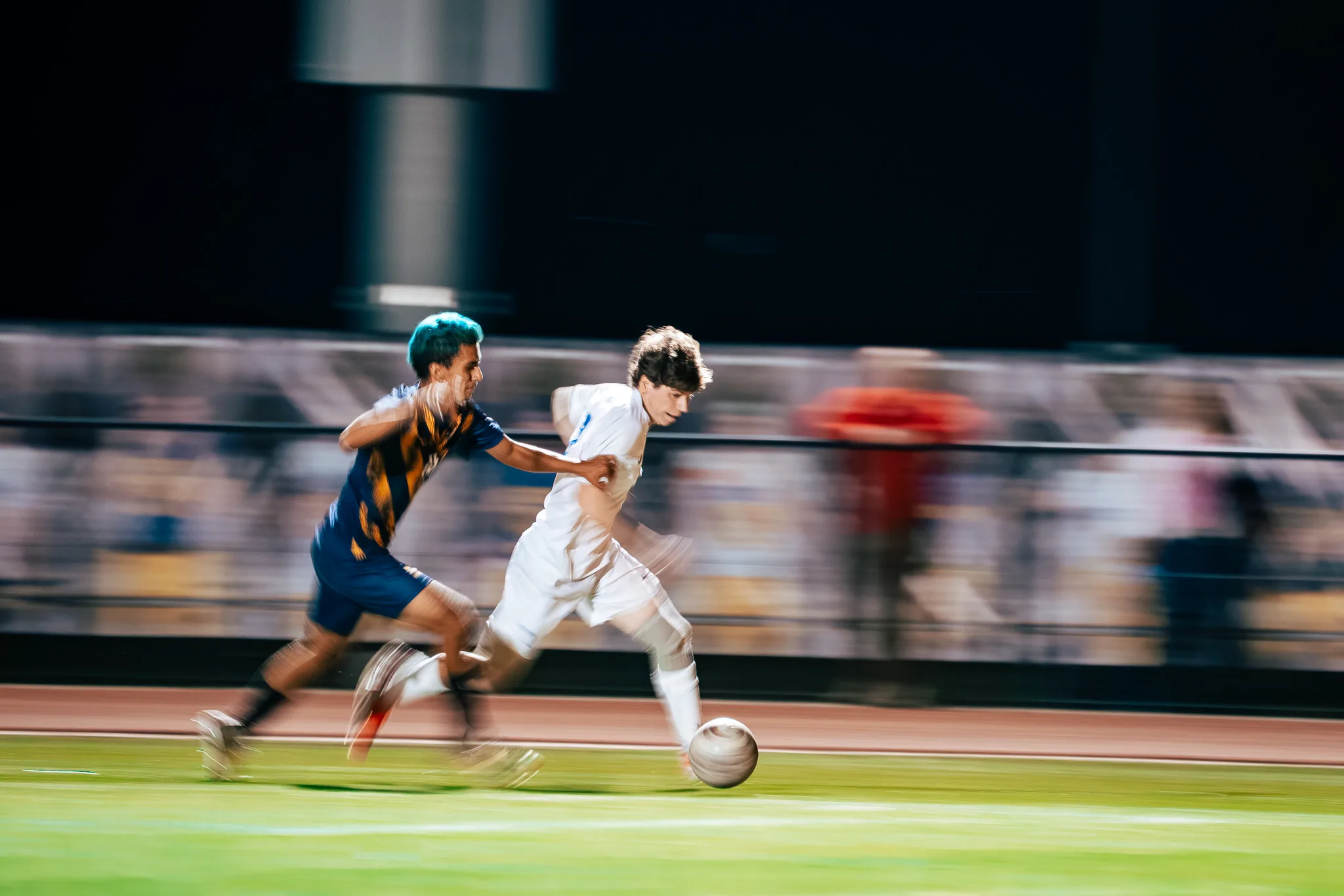 In a streak of motion, a Centaurus player dribbles along the sideline with a Frederick player in close pursuit, the crowd smeared behind them