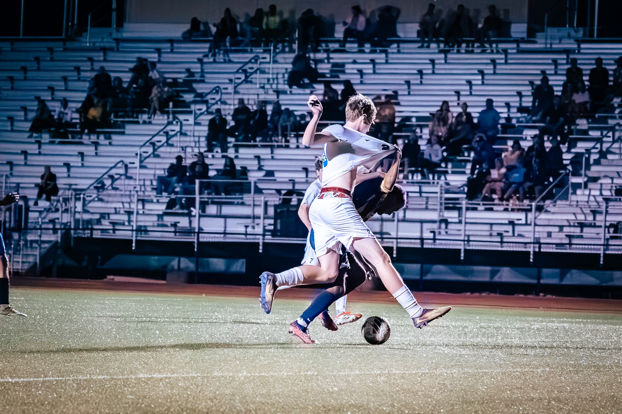 A Centaurus player's jersey is pulled up behind him as he and a Frederick player scramble for the ball, the bleachers filled behind them