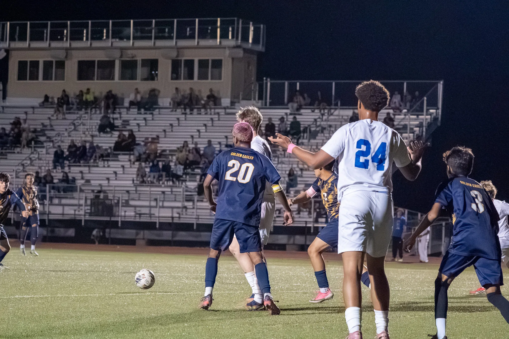 Centaurus number 24 and Frederick numbers 20 and 3 turn to follow the ball as it rolls loose on the turf, the bleachers and press box behind them