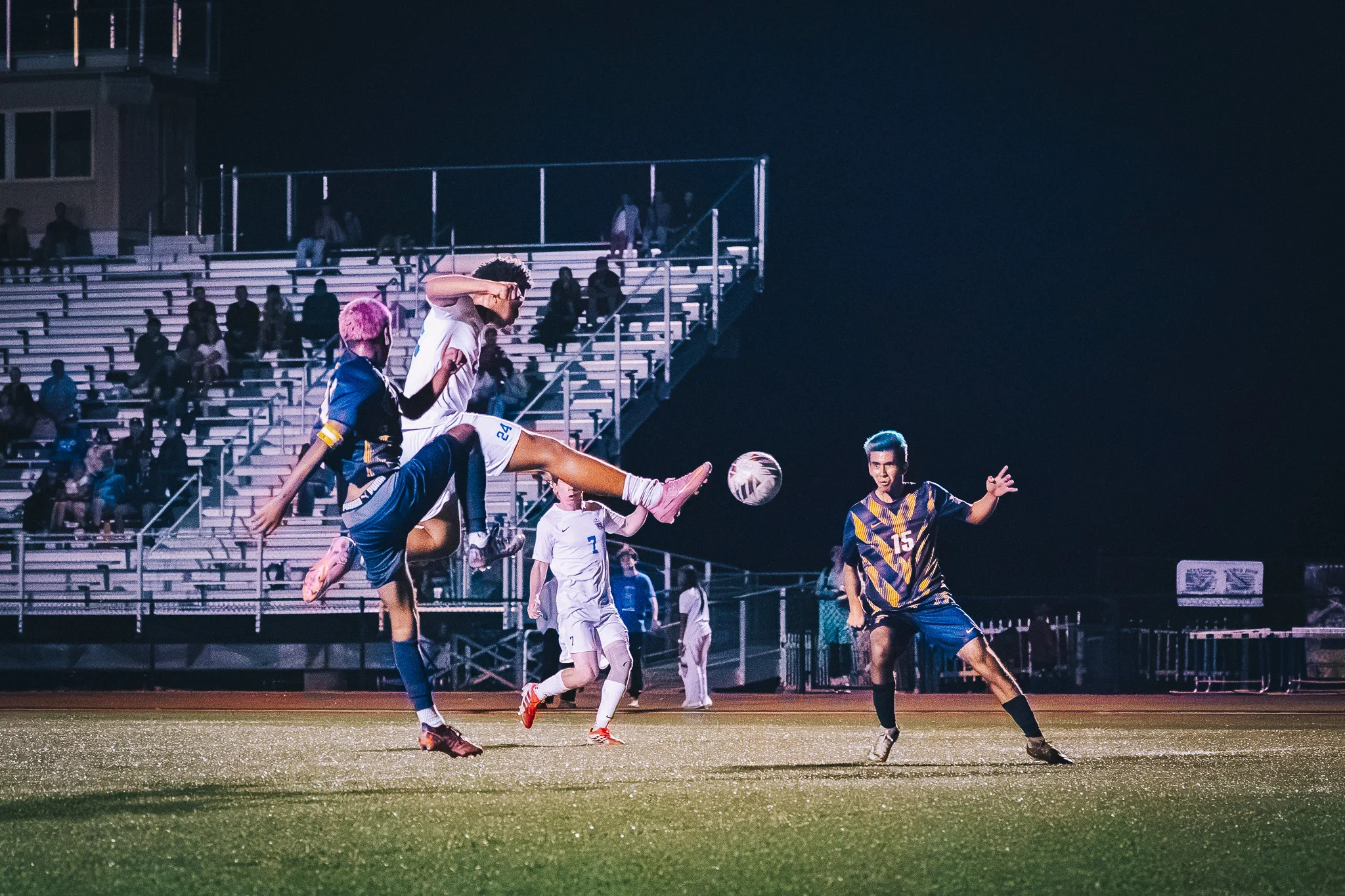 Centaurus number 24 swings a leg high at the ball over a Frederick player with pink hair as Centaurus number 7 runs in and Frederick number 15 watches from the right