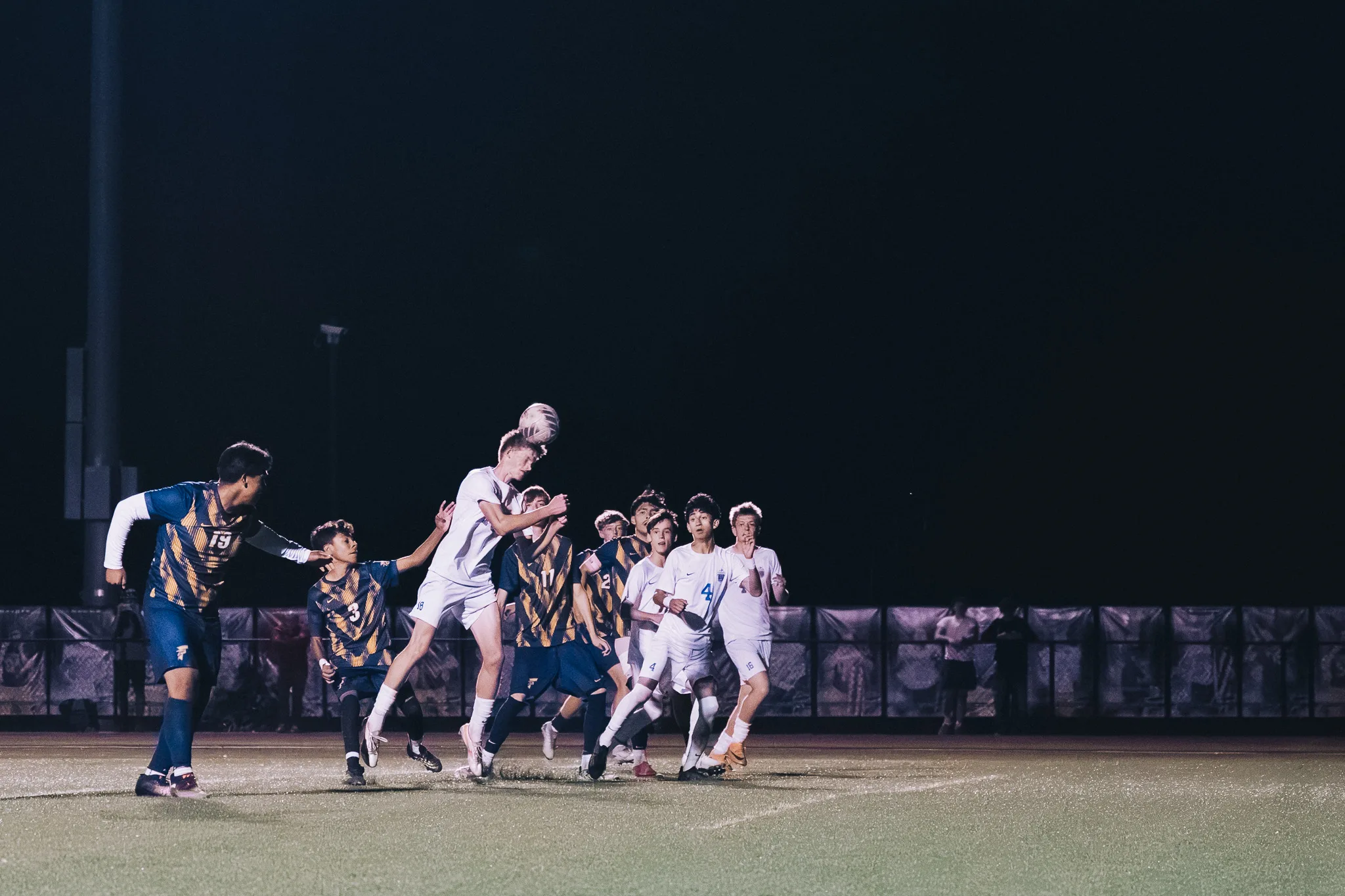 At night, a tall Centaurus player rises above a crowd in front of the goal to head the ball, Frederick number 3 and Centaurus number 4 among the players beneath him