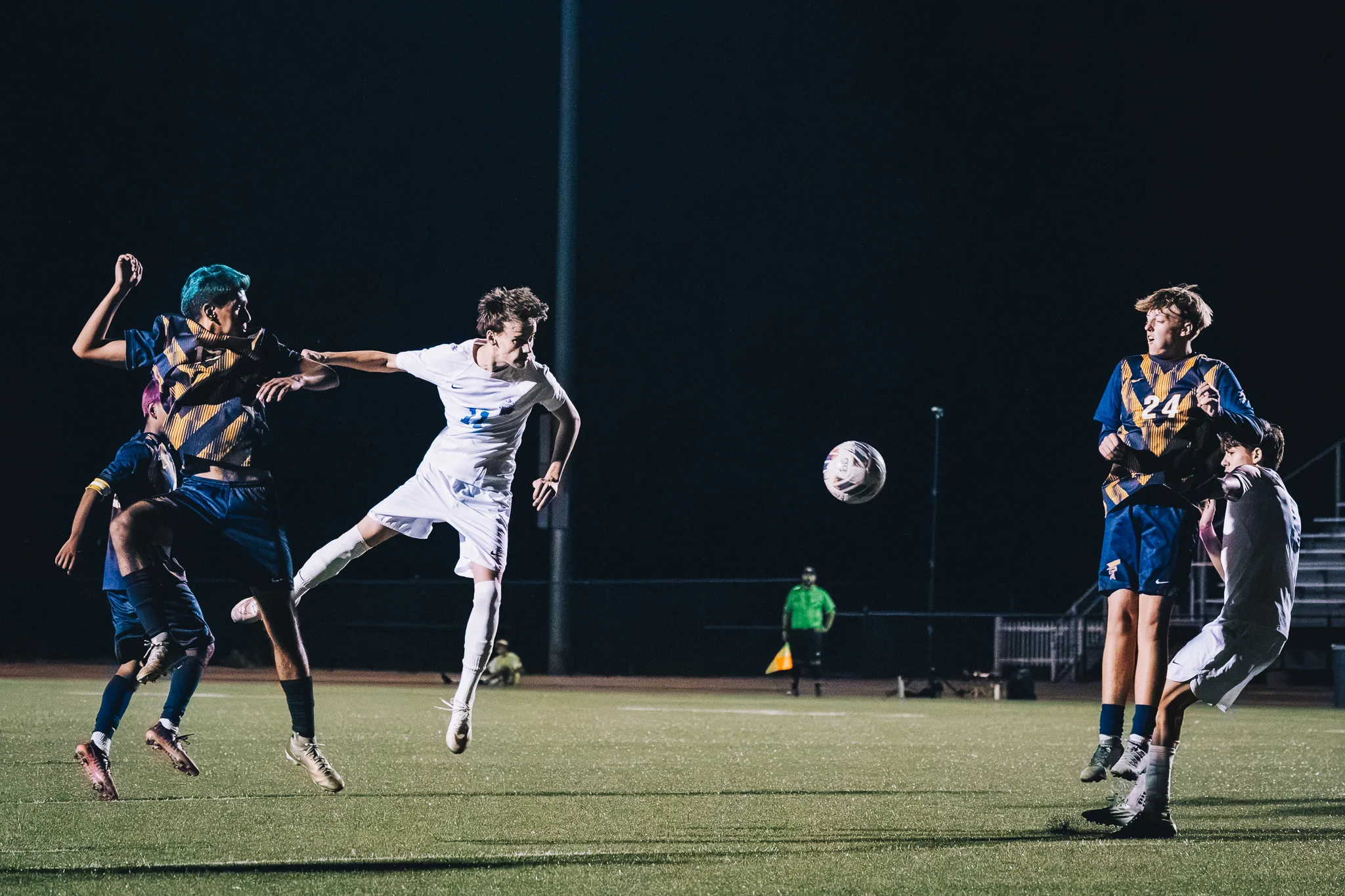 As the ball flies off to the right, a Centaurus player leaps beside two Frederick players, with Frederick number 24 and an assistant referee in green looking on