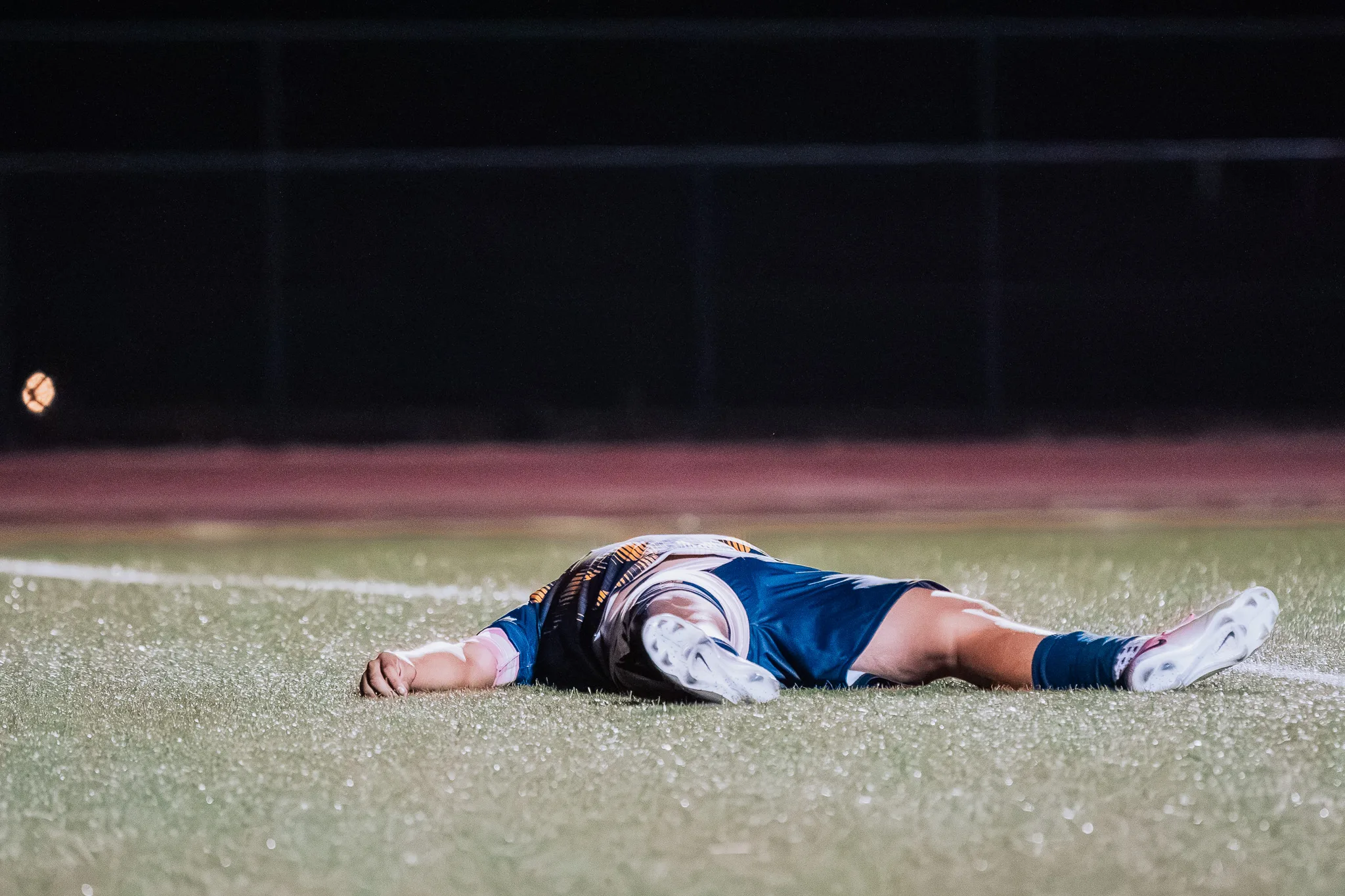 At night, a Frederick player lies flat on his back on the turf with his arms and legs spread
