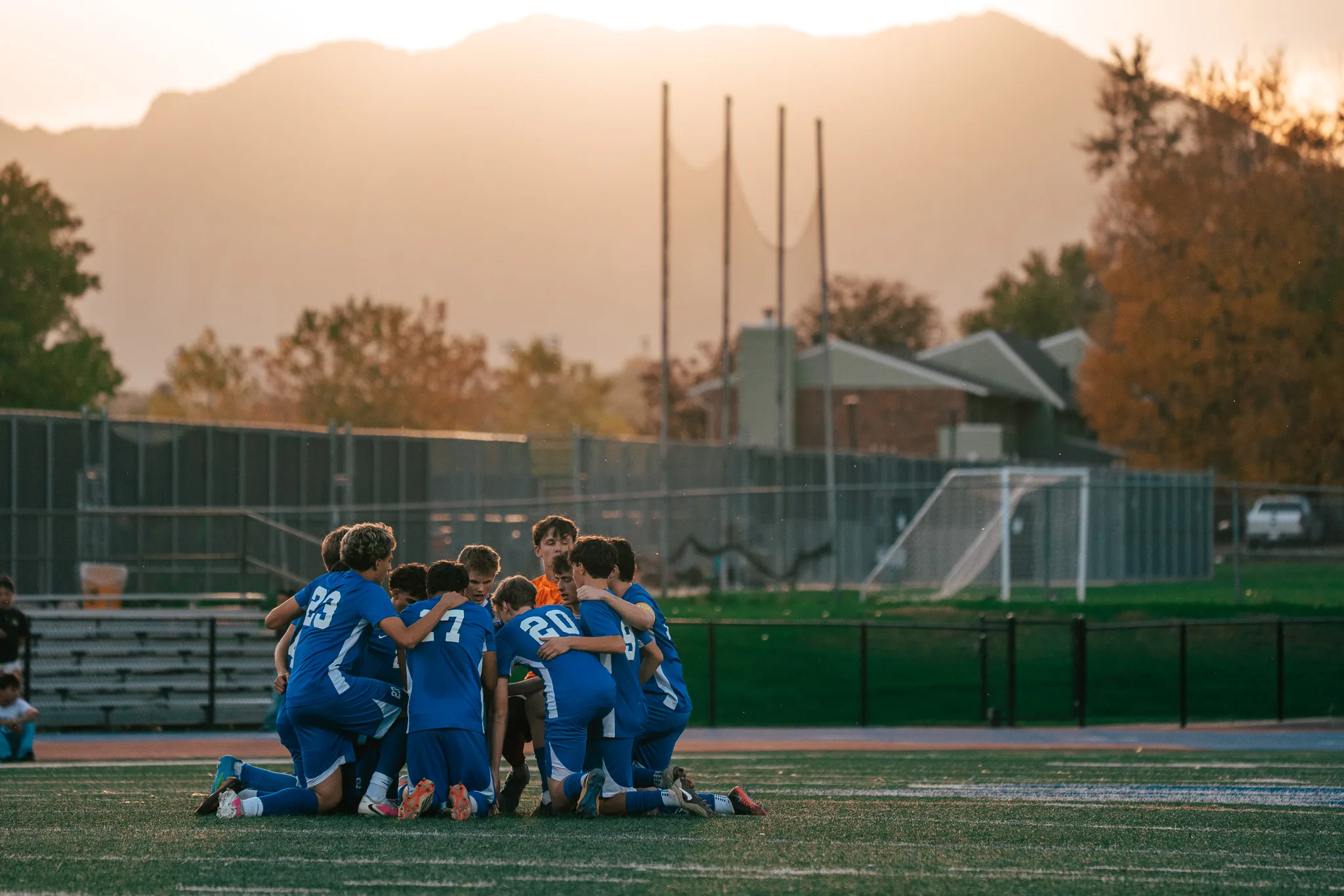 Centaurus players kneel in a tight huddle with the goalkeeper in orange among them, the mountains glowing behind